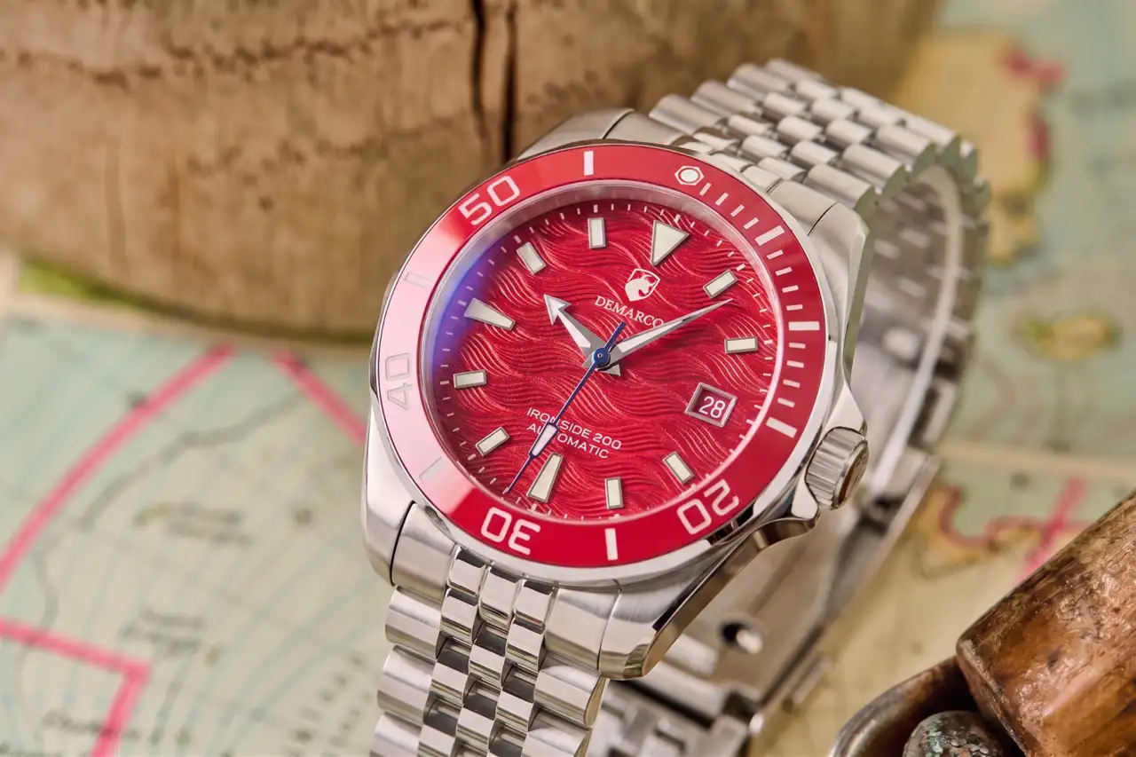 The DeMarco Ironside 200 with a red wave dial and red bezel on a steel jubilee bracelet, resting on an old nautical chart