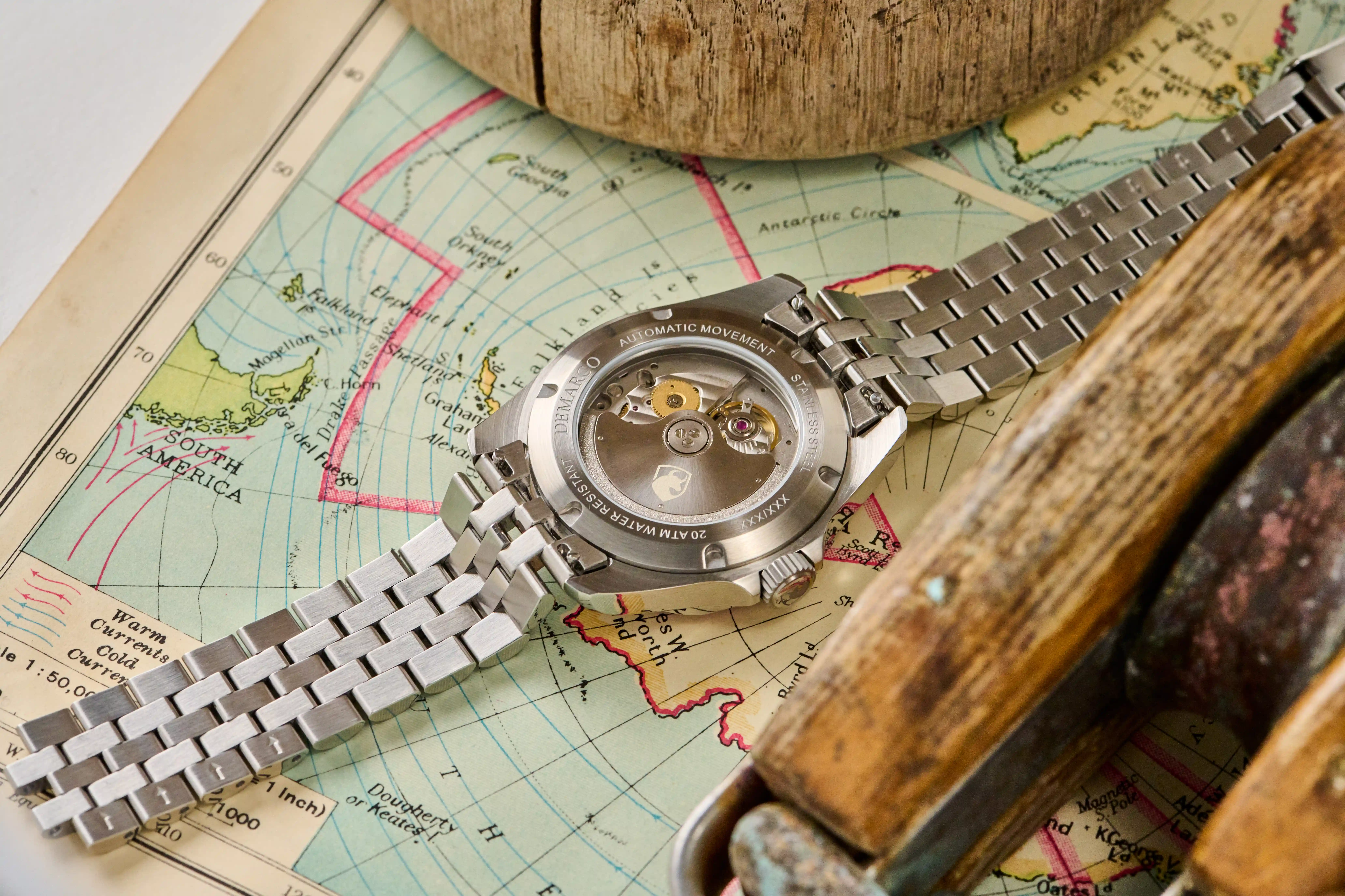 A DeMarco watch lying face down on an antique nautical chart, its movement visible through the display caseback