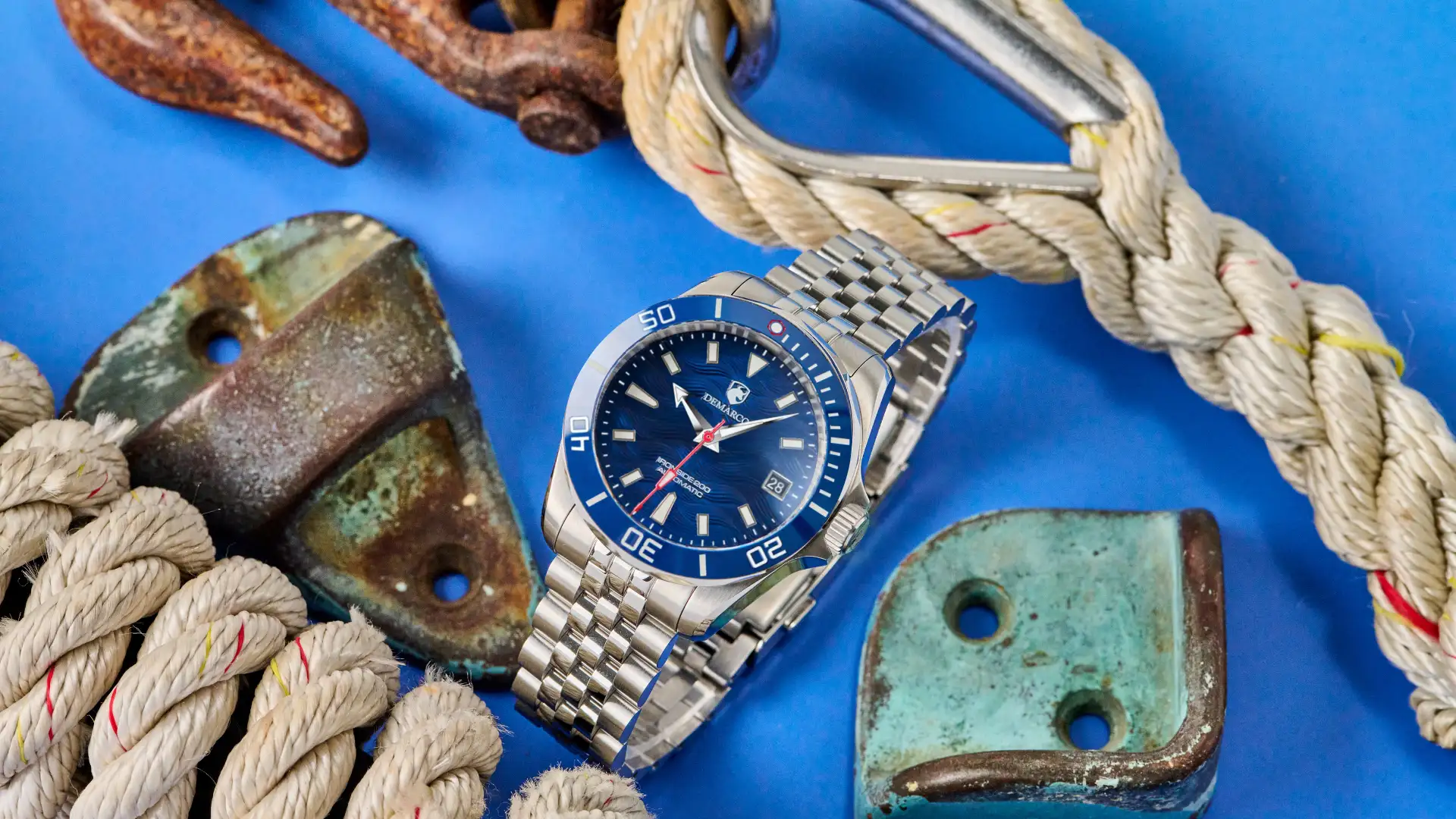 The DeMarco Ironside 200 with a blue dial on a steel bracelet, styled on a blue background with marine rope and weathered brass fittings