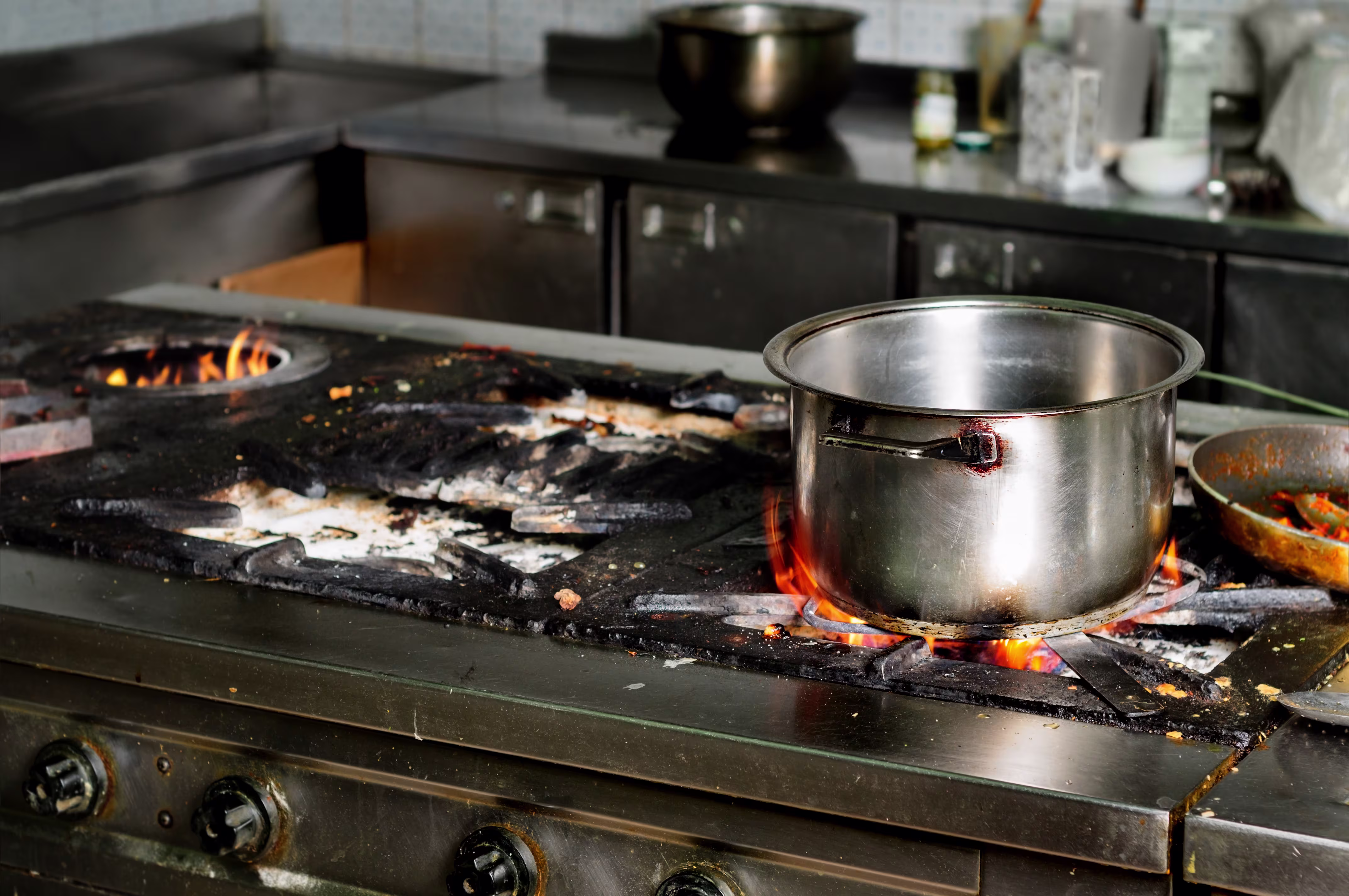 Stainless steel pot heating on a commercial gas stove with visible flames in a kitchen.