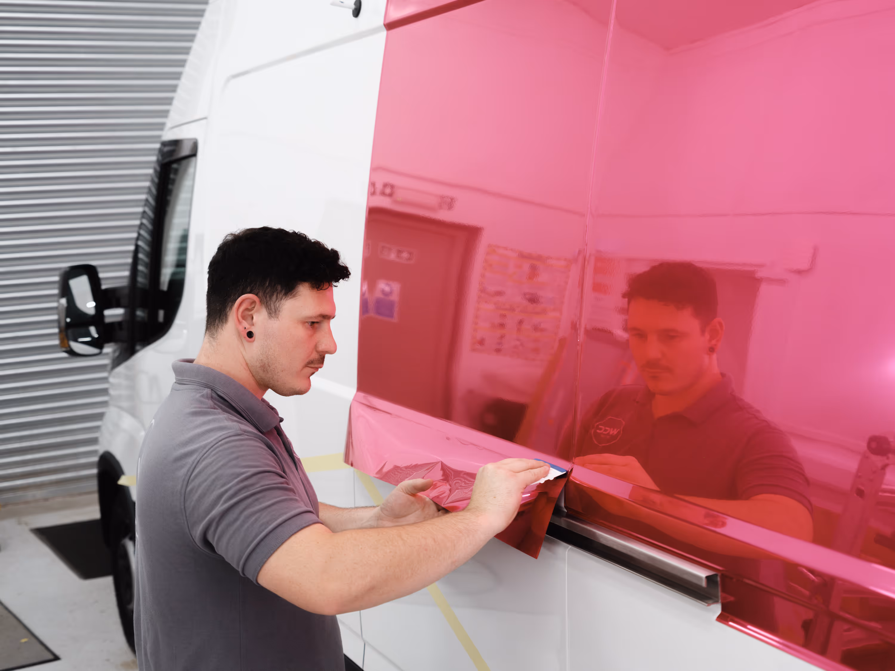 A WCC worker applying a chrome pink wrap to a van.