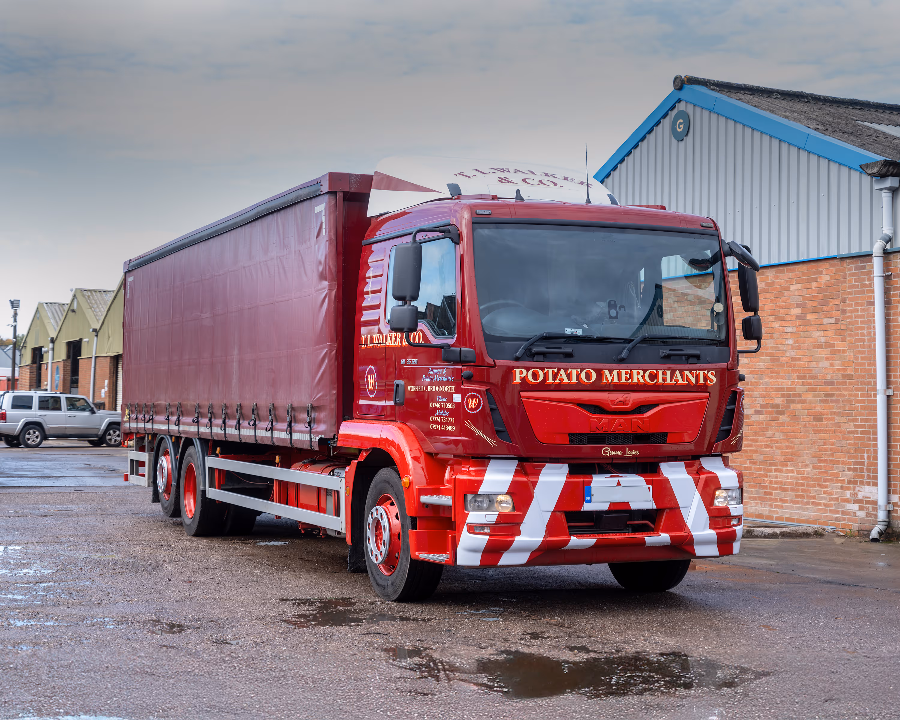 Red T. L. Walker & Co. truck with 'Potato Merchants' signage parked near brick and industrial buildings on a wet surface.