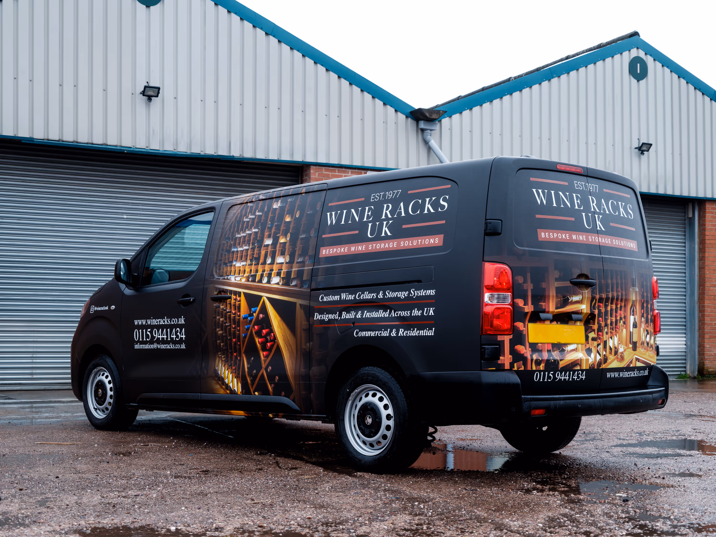 Black van parked outside warehouse with 'Wine Racks UK' branding and images of wine racks filled with bottles.