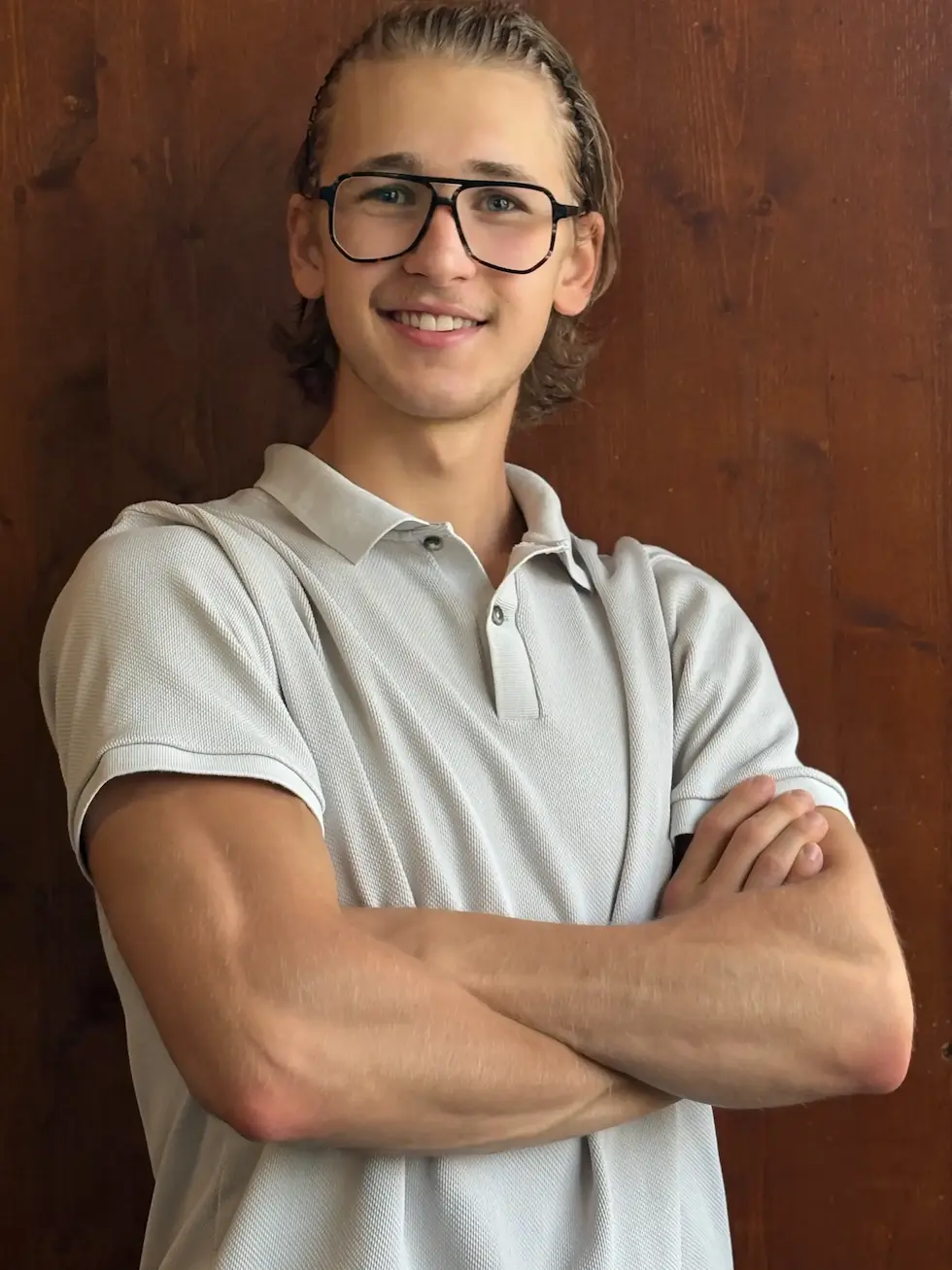 Oscar Straßburg mit verschränkten Armen vor Holz-Hintergrund, selbstbewusstes Coaching-Portrait