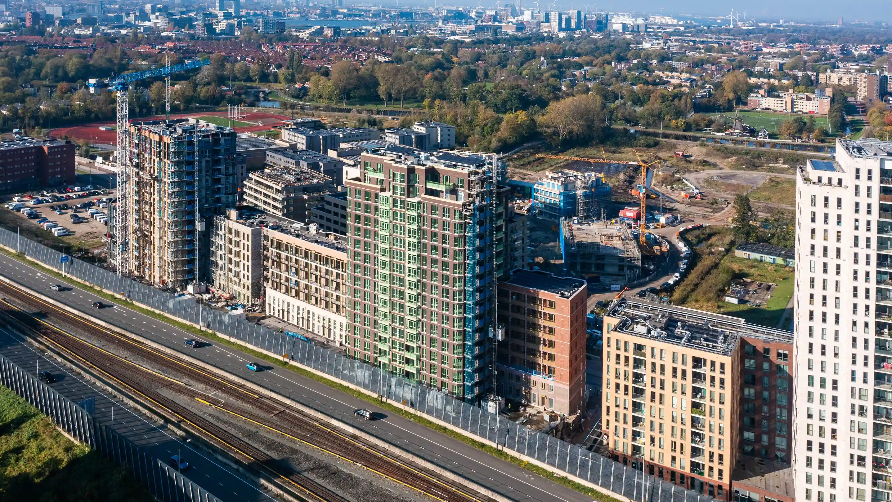 Aerial view of residential buildings under construction near a highway in the Netherlands, featuring acoustic louvres for noise reduction and ventilation.