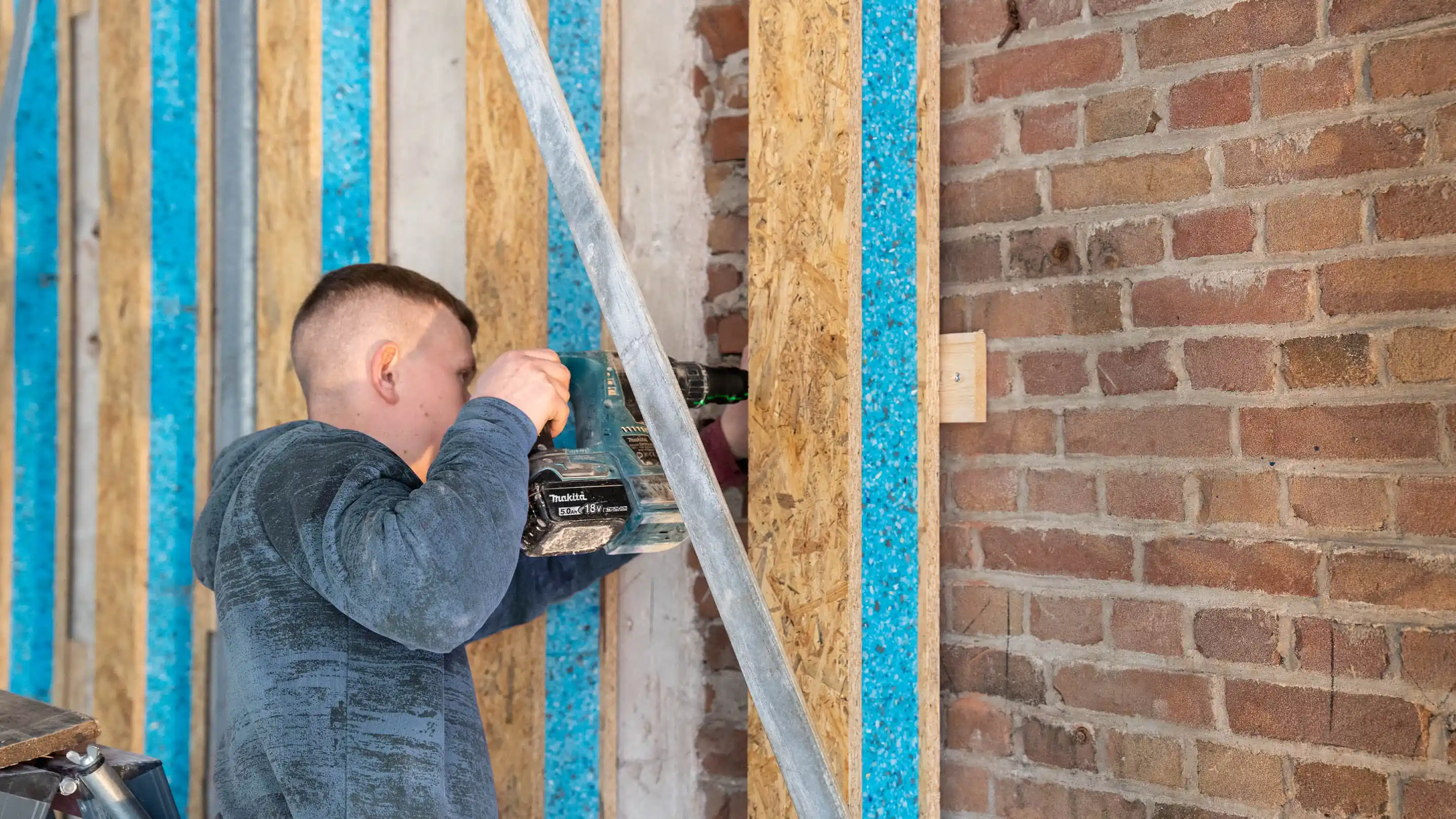 Installer applying Merford Akoestikon sound insulation material to a wall structure for improved acoustic performance.