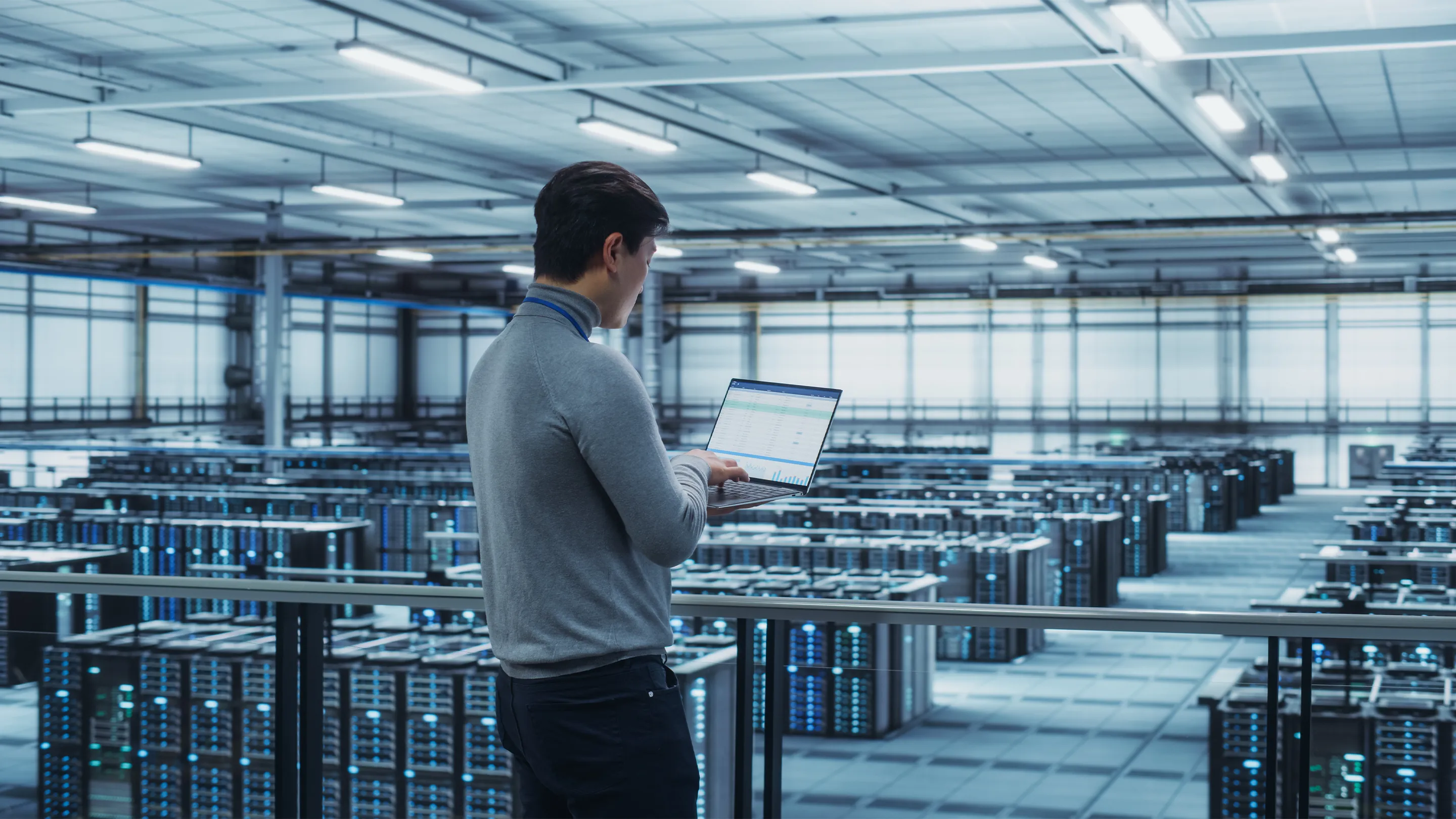 Ingenieur inspecteert de infrastructuur van een datacenter terwijl hij aan een laptop werkt in een grote serverhal.