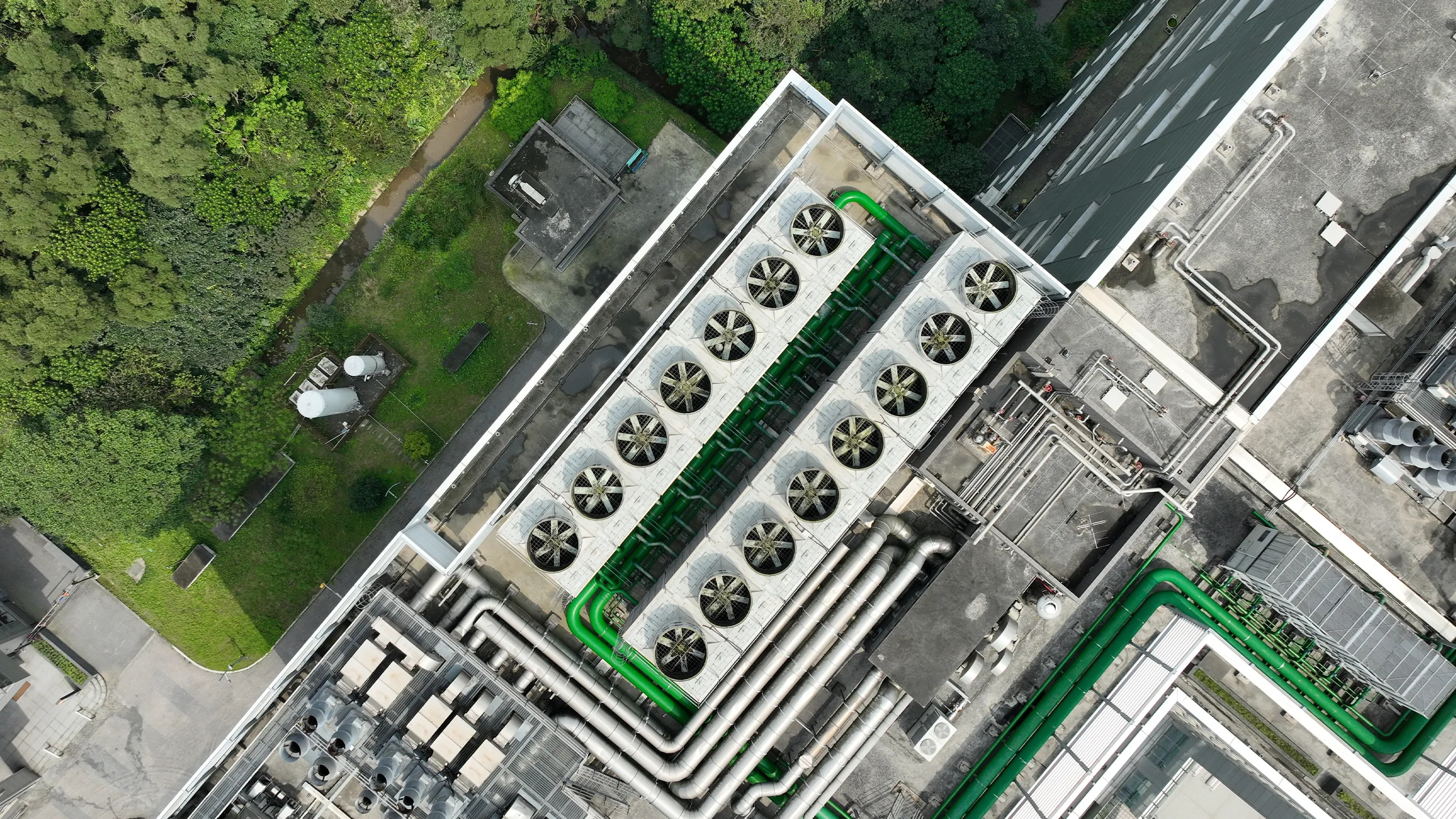Aerial view of rooftop HVAC and cooling installations at a data centre, showing large ventilation units, pipework and surrounding greenery.
