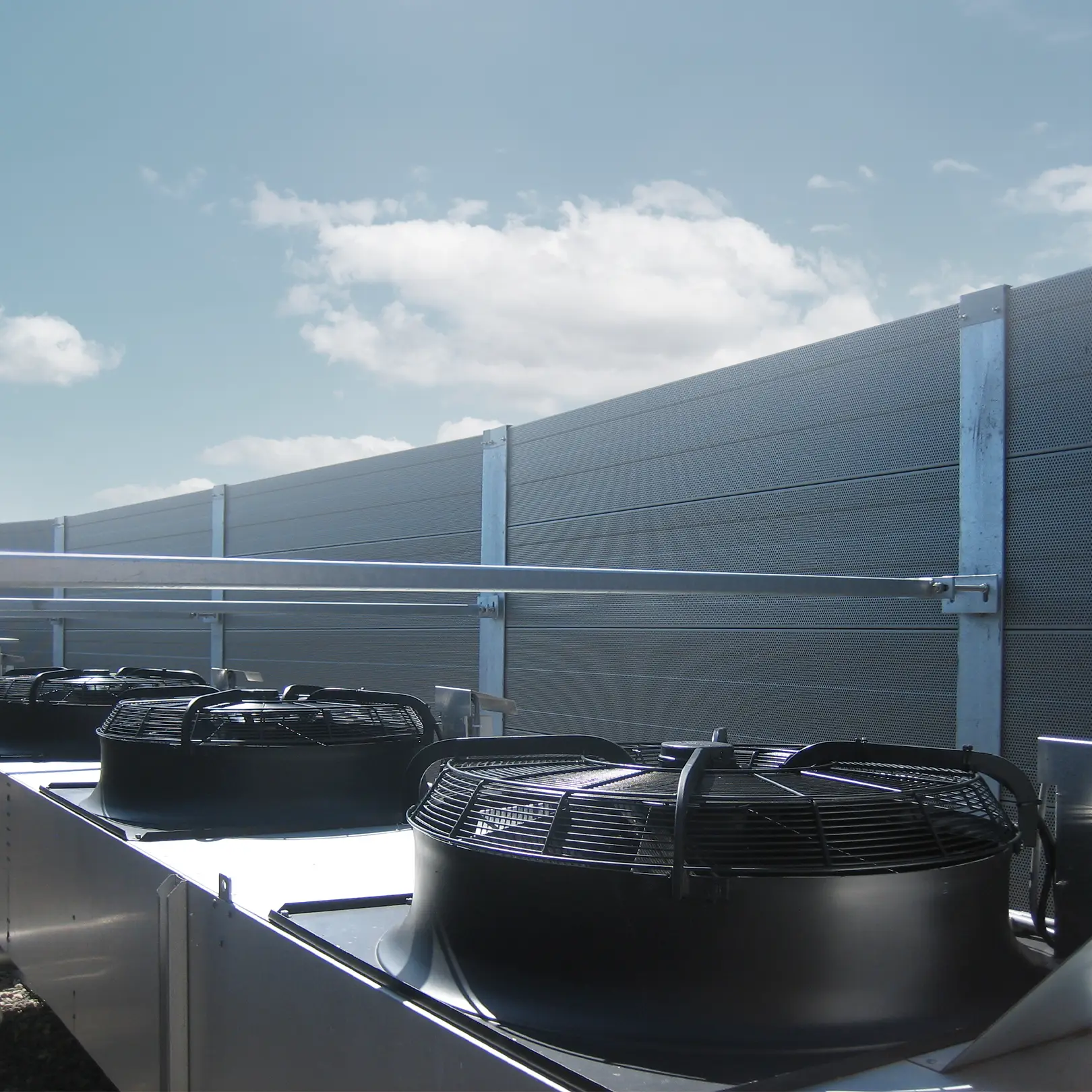 Koelinstallaties met ventilatoren op een dakopstelling achter een akoestisch geluidscherm.