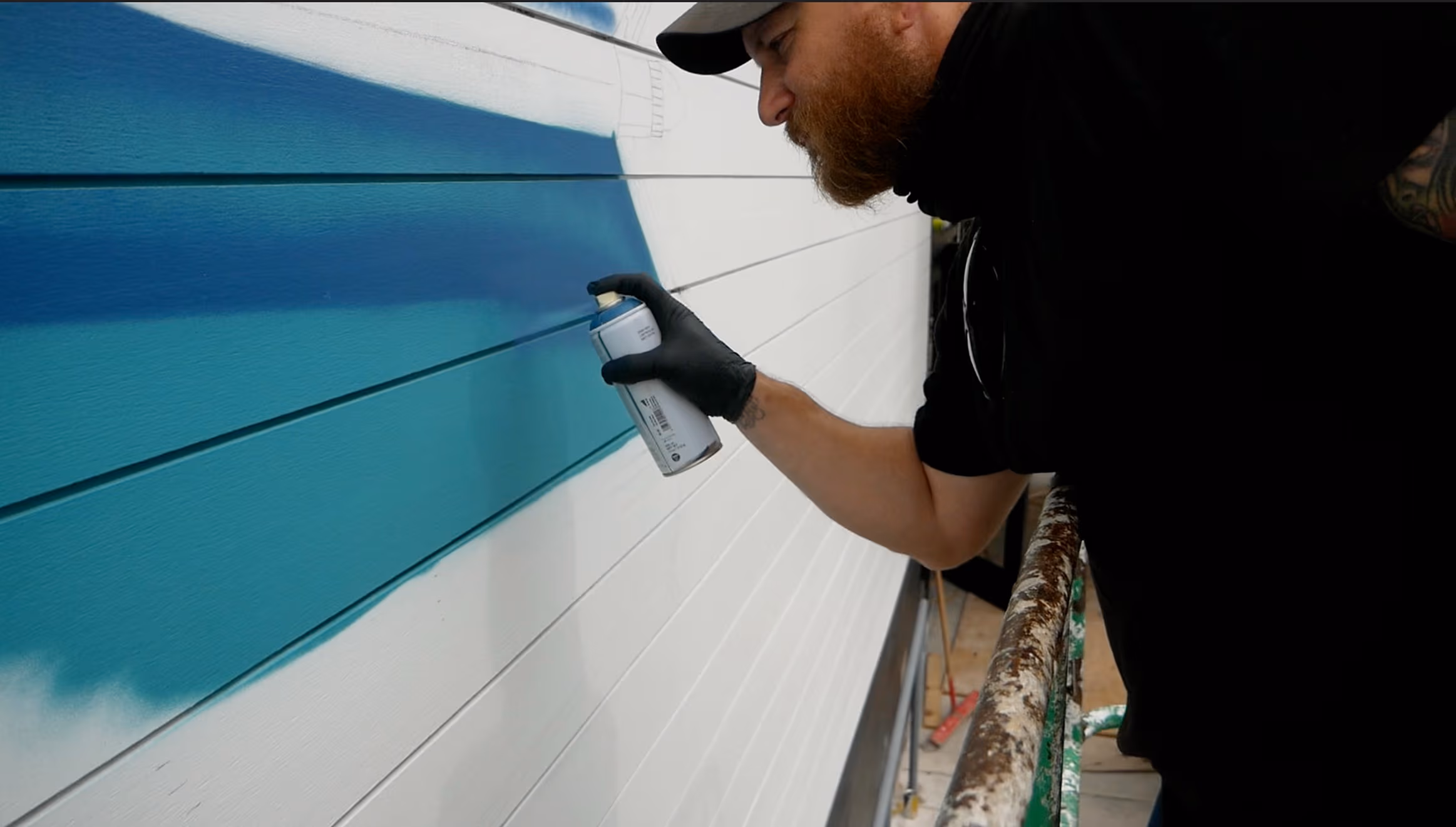 A medium shot of Mammoth Mural's co-founder spray painting a mural
