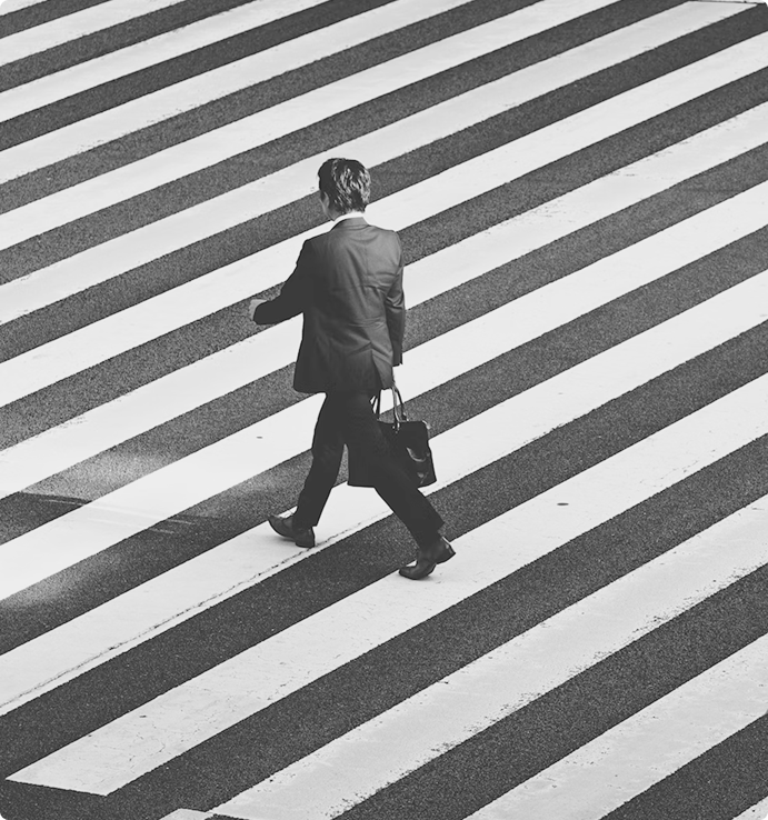 Man in a suit carrying a bag walking across a wide striped pedestrian crosswalk.