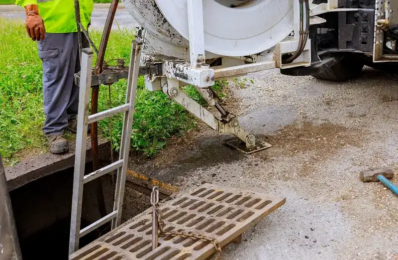 Worker in safety gear next to open manhole with ladder, urban utility maintenance