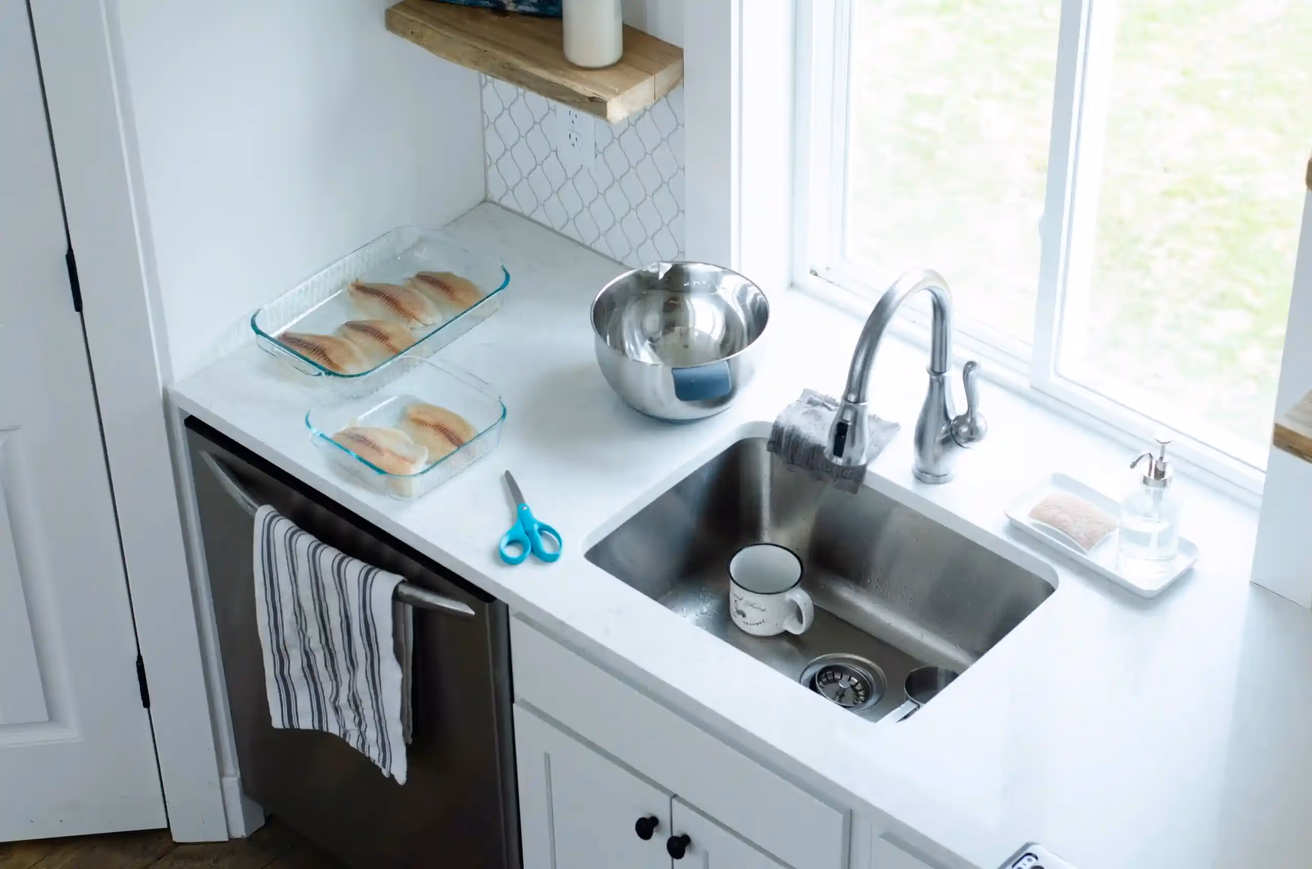  A bright, high-angle shot provides a view of a clean kitchen counter featuring a stainless steel sink with a modern faucet. On the white countertop, there are two glass baking dishes