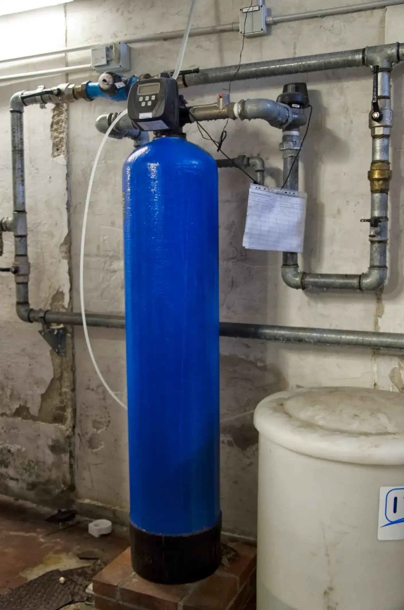 A tall, bright blue water softener tank with a control valve in a utility room.