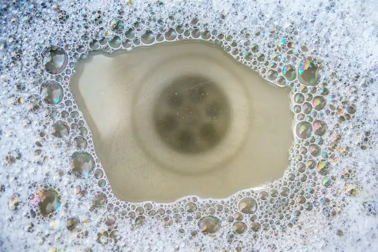A close-up, high-angle view of a dirty drain in a sink surrounded by colorful soap bubbles.