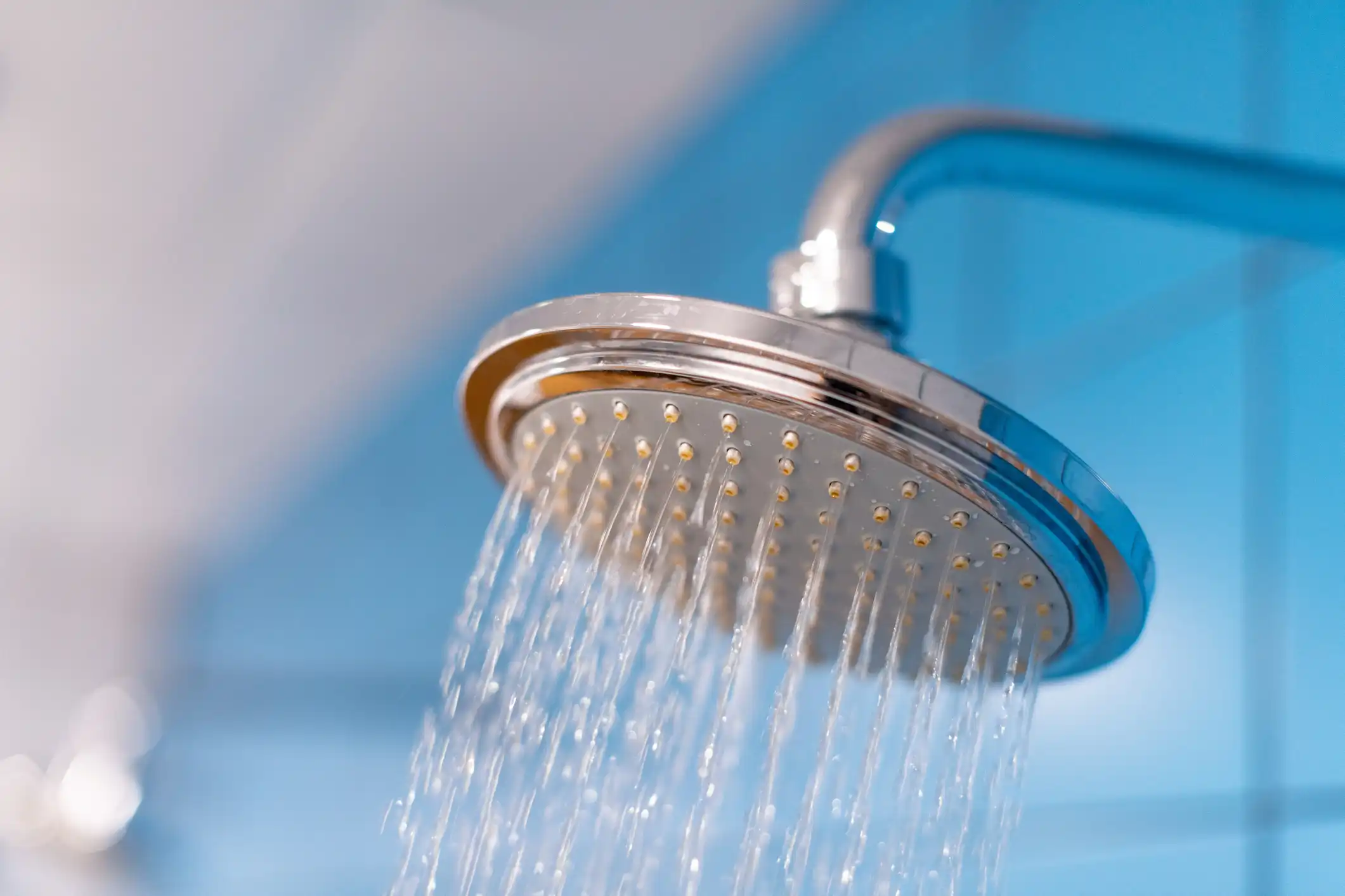 A hand in a blue rubber glove uses a sponge to clean a shiny kitchen faucet and a white sink.
