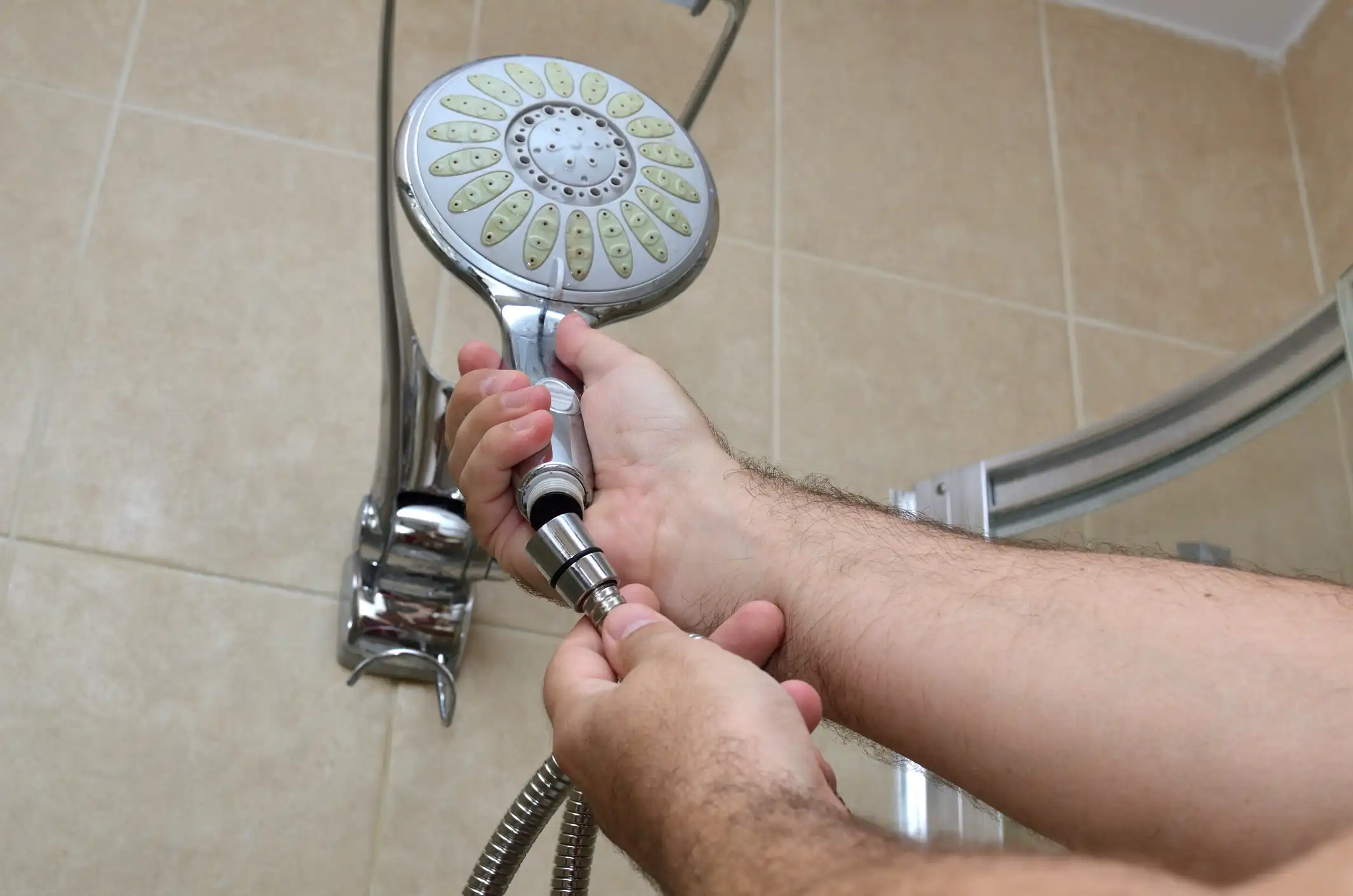 A close-up of a person's hands wearing blue gloves, using a tool to cut a white plastic pipe against a blurred background.