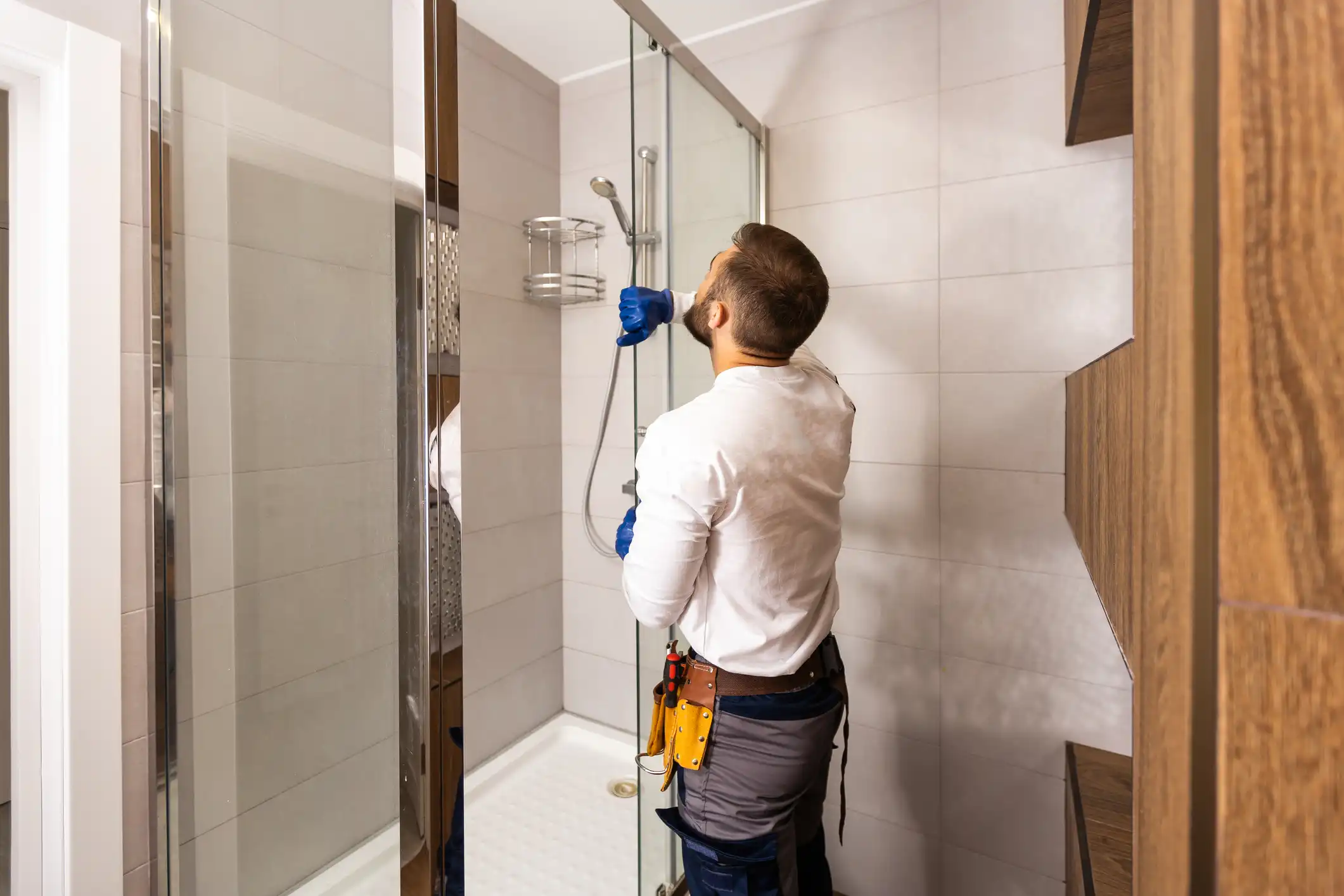 A plumber in a hard hat and blue gloves inspects the pipes and gauges on a boiler system in a home.