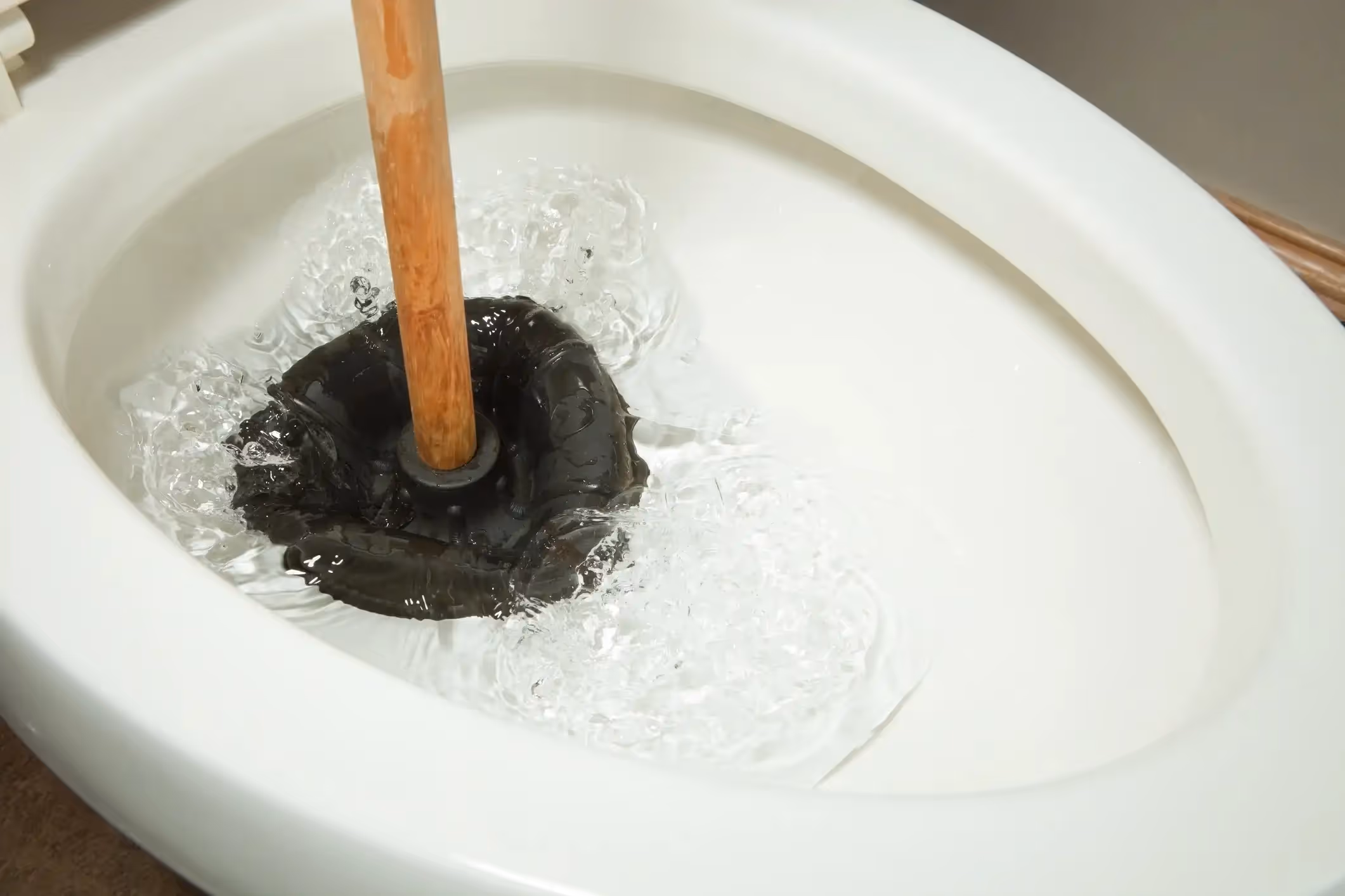 A plumber lies on his back under a sink, using a wrench to work on the pipes.