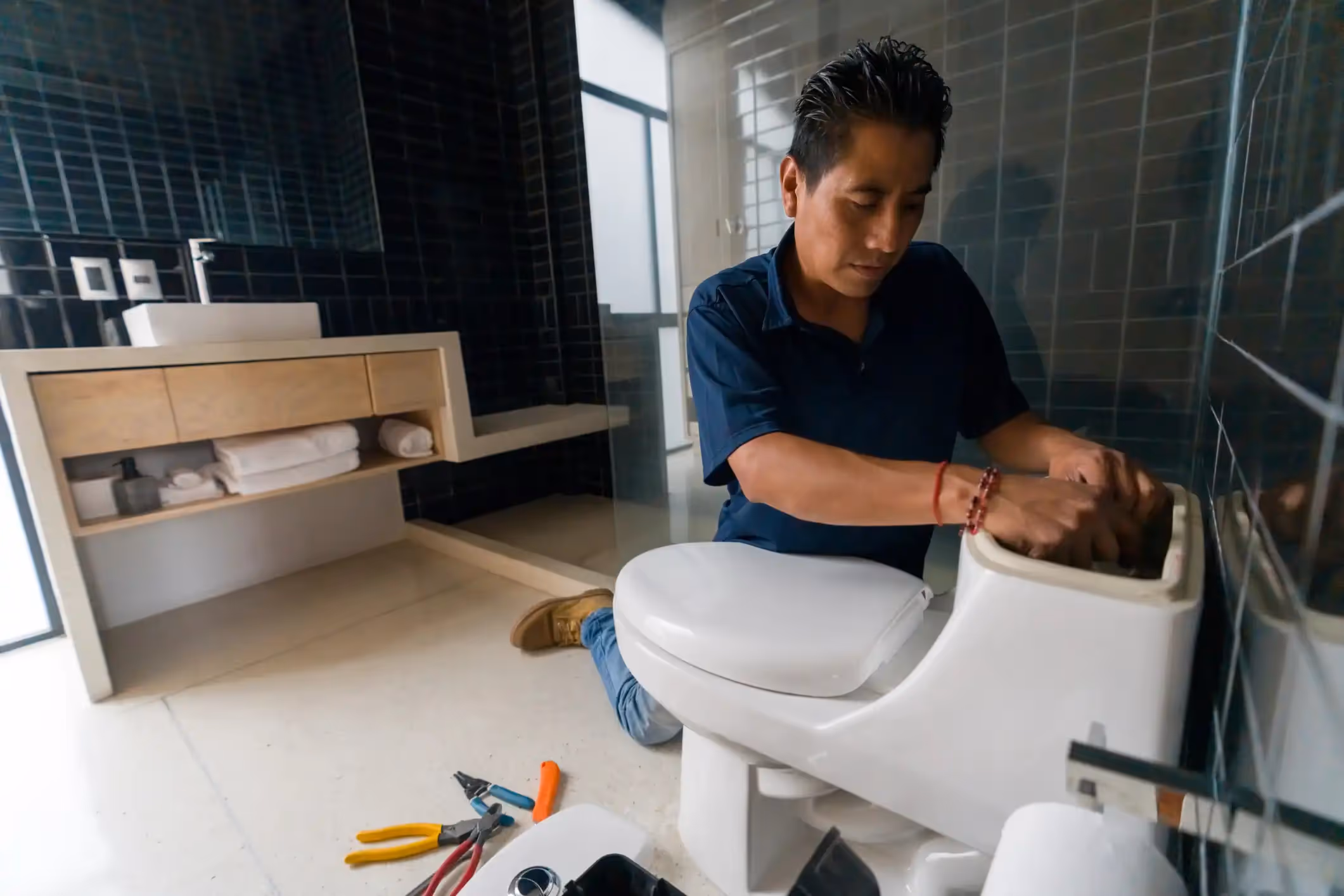 A plumber's gloved hand adjusts a pipe under a sink.