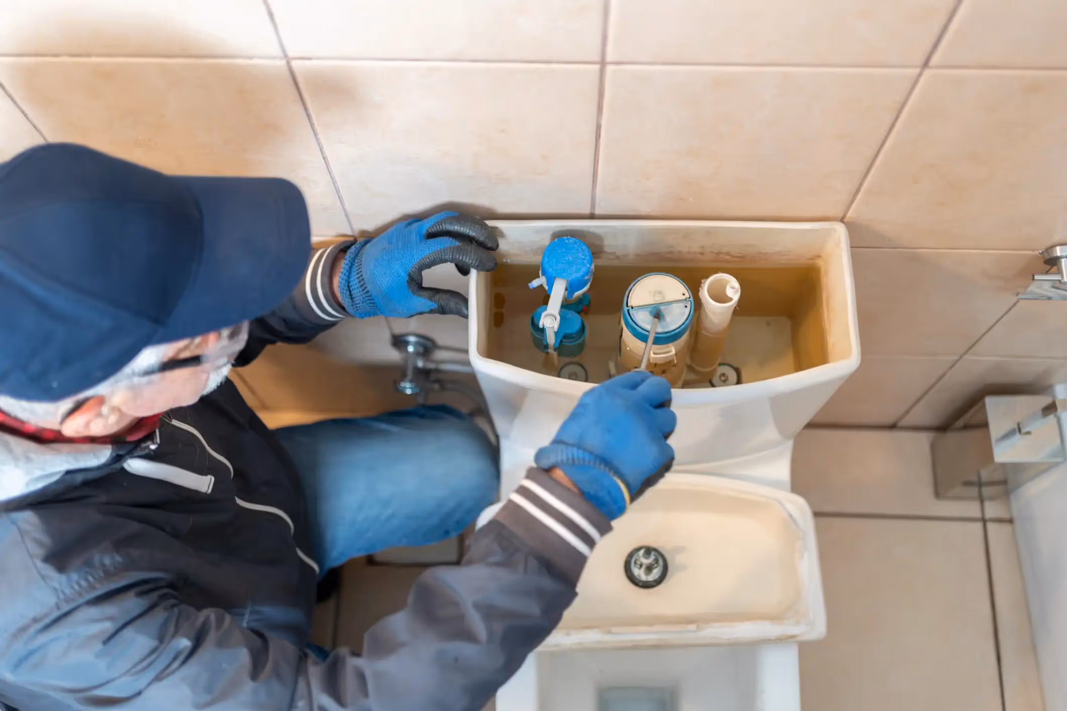 A plumber's hands in gloves use a wrench to tighten a pipe under a kitchen sink.