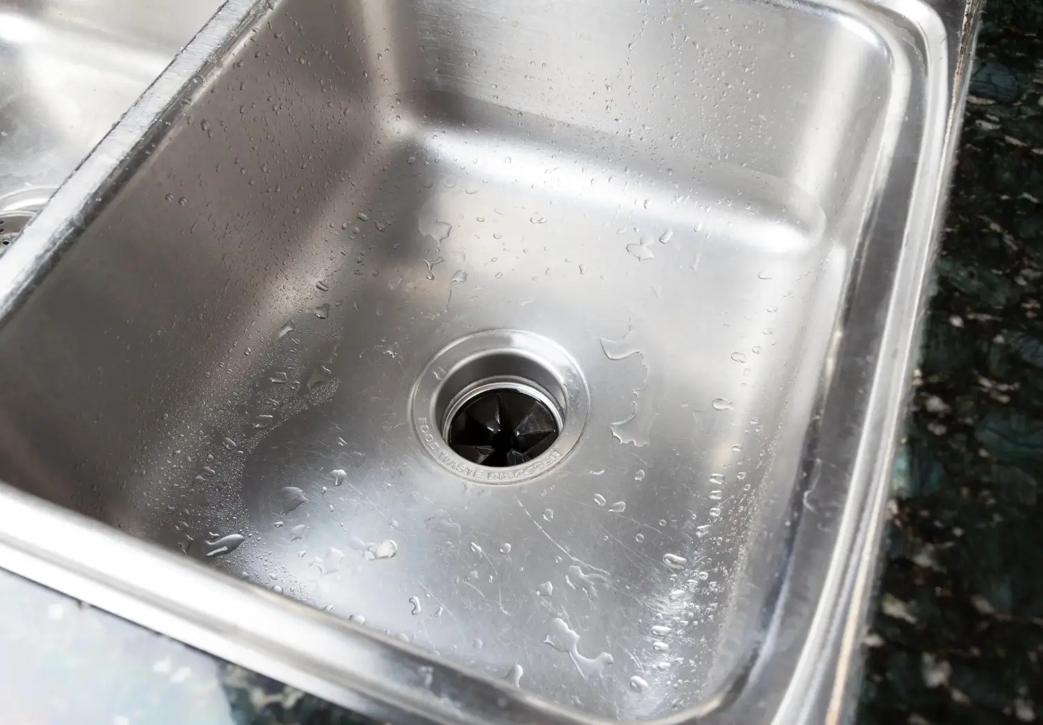 A wide view of a stainless steel kitchen sink with a prominent food waste disposer drain.