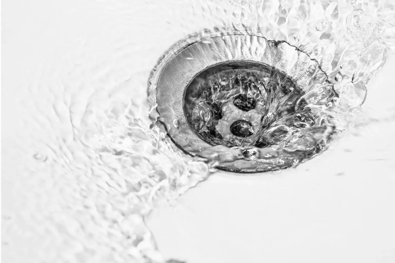A close-up of a clean metal sink drain surrounded by water and bubbles.
