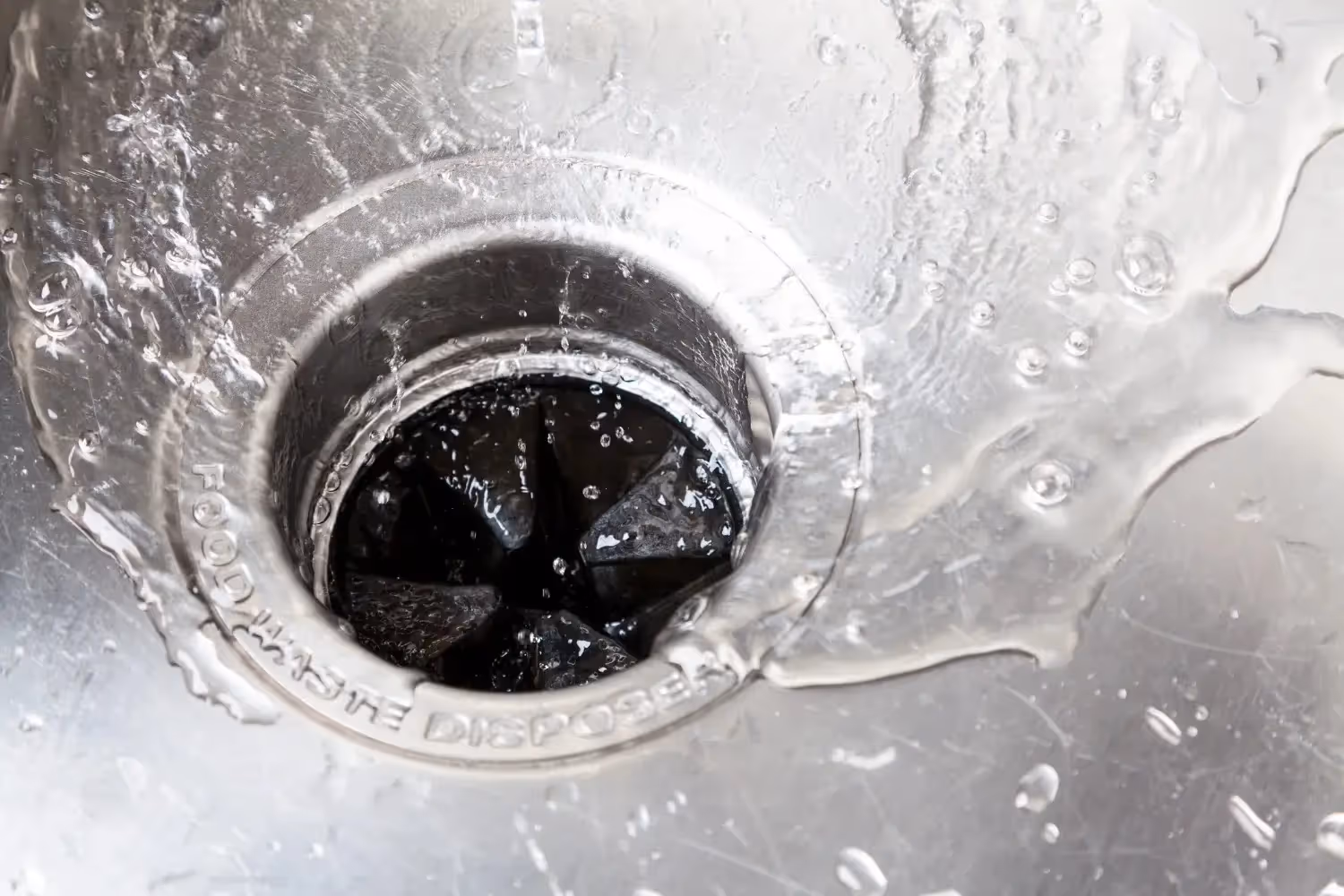 Water flowing into a kitchen sink drain with a food waste disposer visible below.