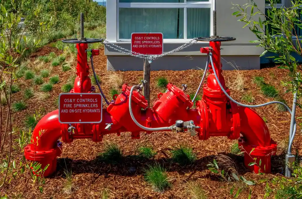 A large, red backflow prevention assembly for fire sprinklers and hydrants, with warning signs attached.
