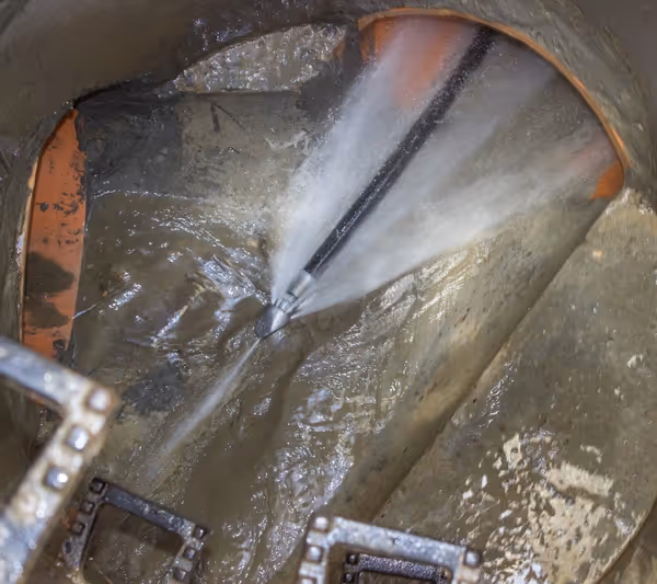 A man uses a hose for hydro jetting to clean a pipe, demonstrating effective pipe maintenance techniques.