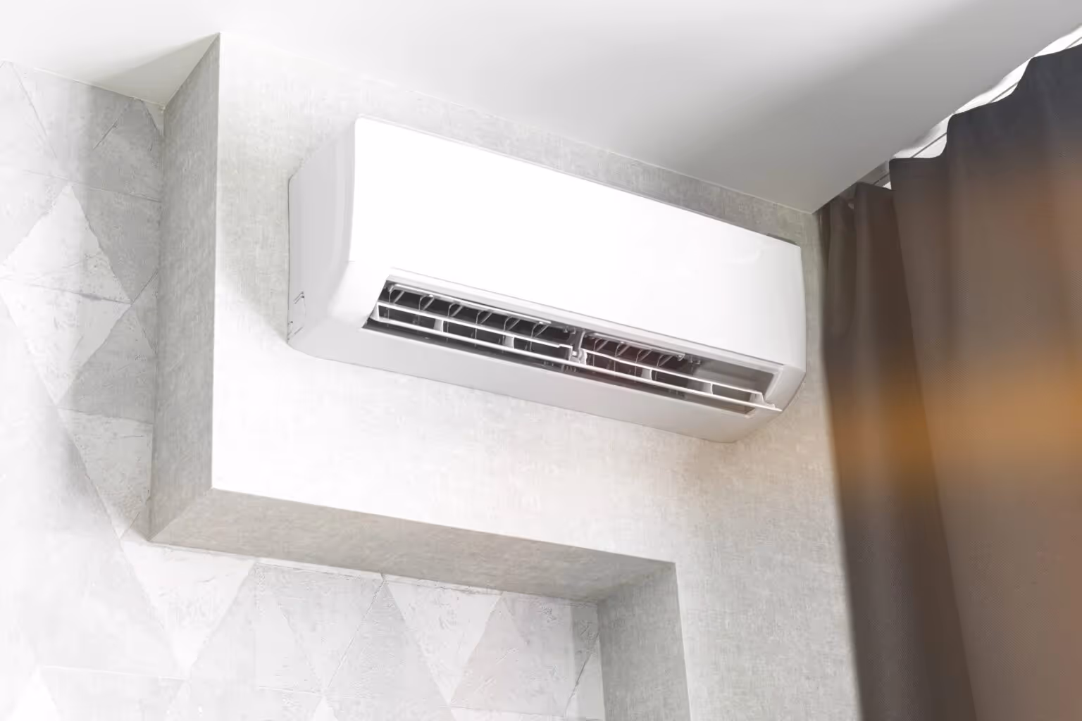 Wall-mounted air conditioner in a modern room, with light gray geometric wallpaper and a dark curtain, conveying a sleek, cool, and comfortable ambiance.