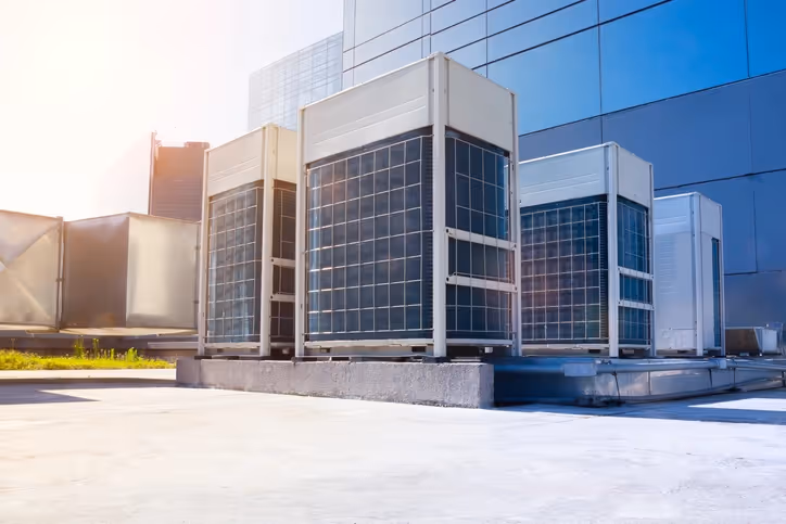 Large industrial air conditioning units are positioned on a rooftop against a modern glass building.