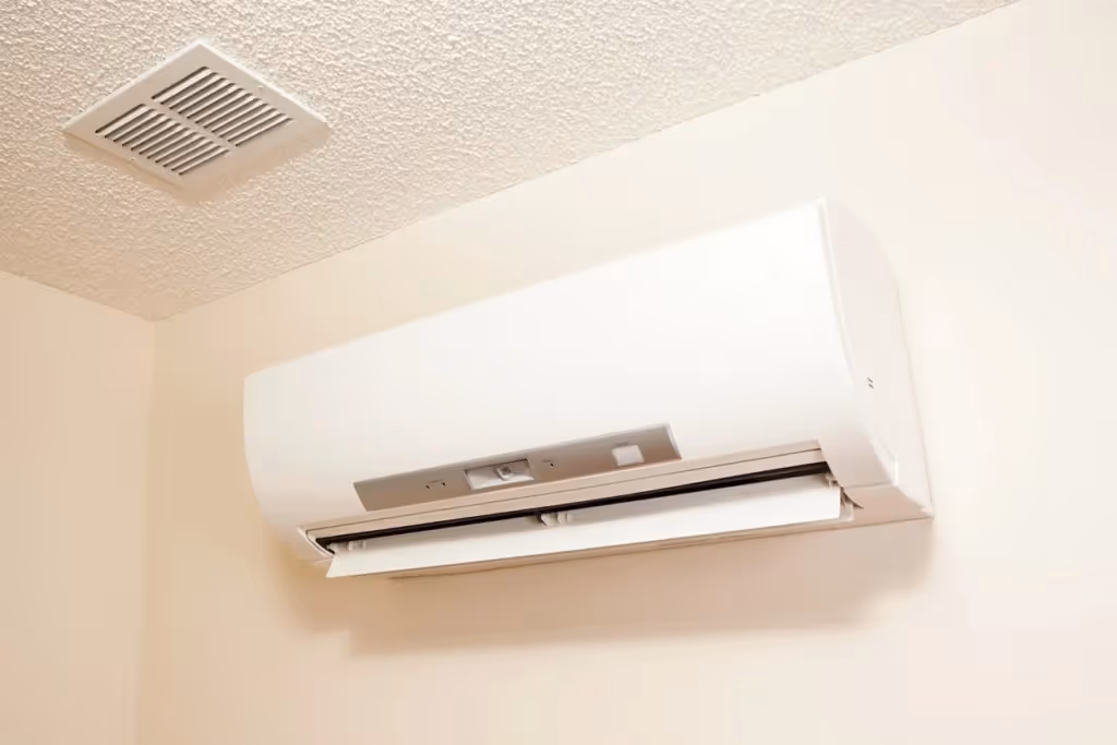 Wall-mounted white air conditioner in a corner, below a vent, blends into the cream-colored walls, conveying a clean and functional environment.