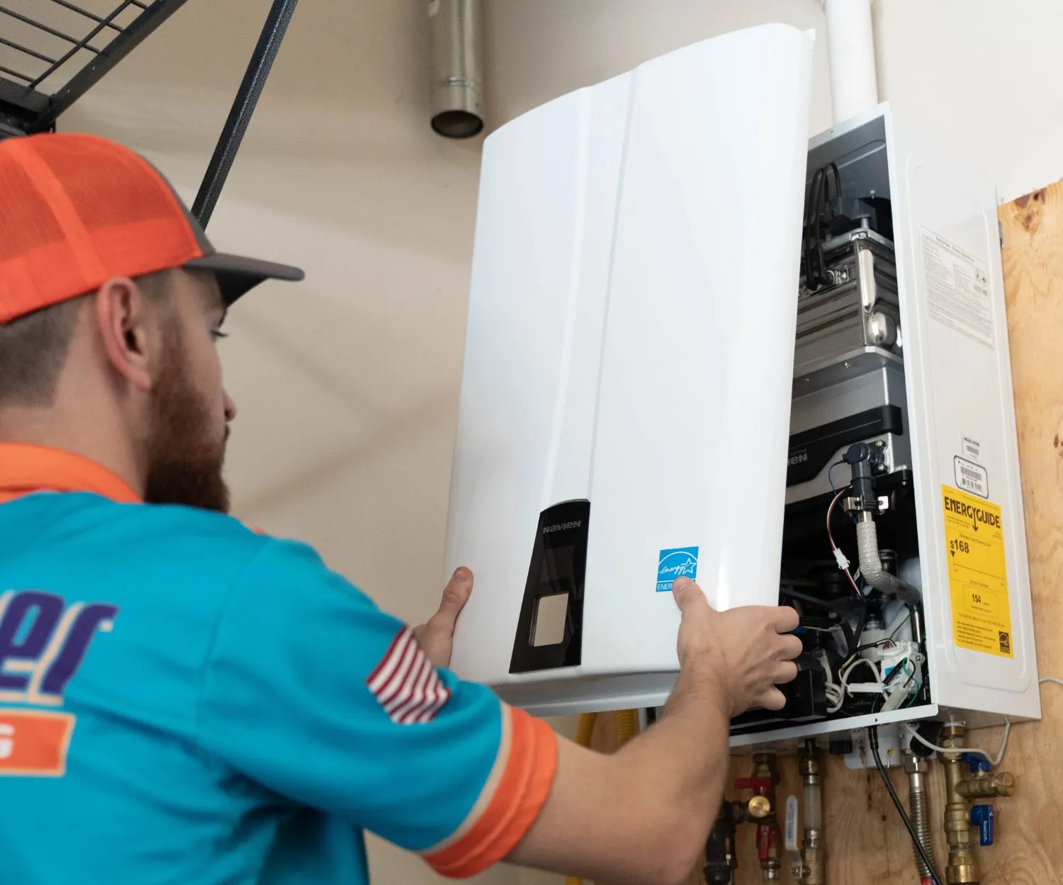 A plumber wearing an orange hat works on a tankless water heater