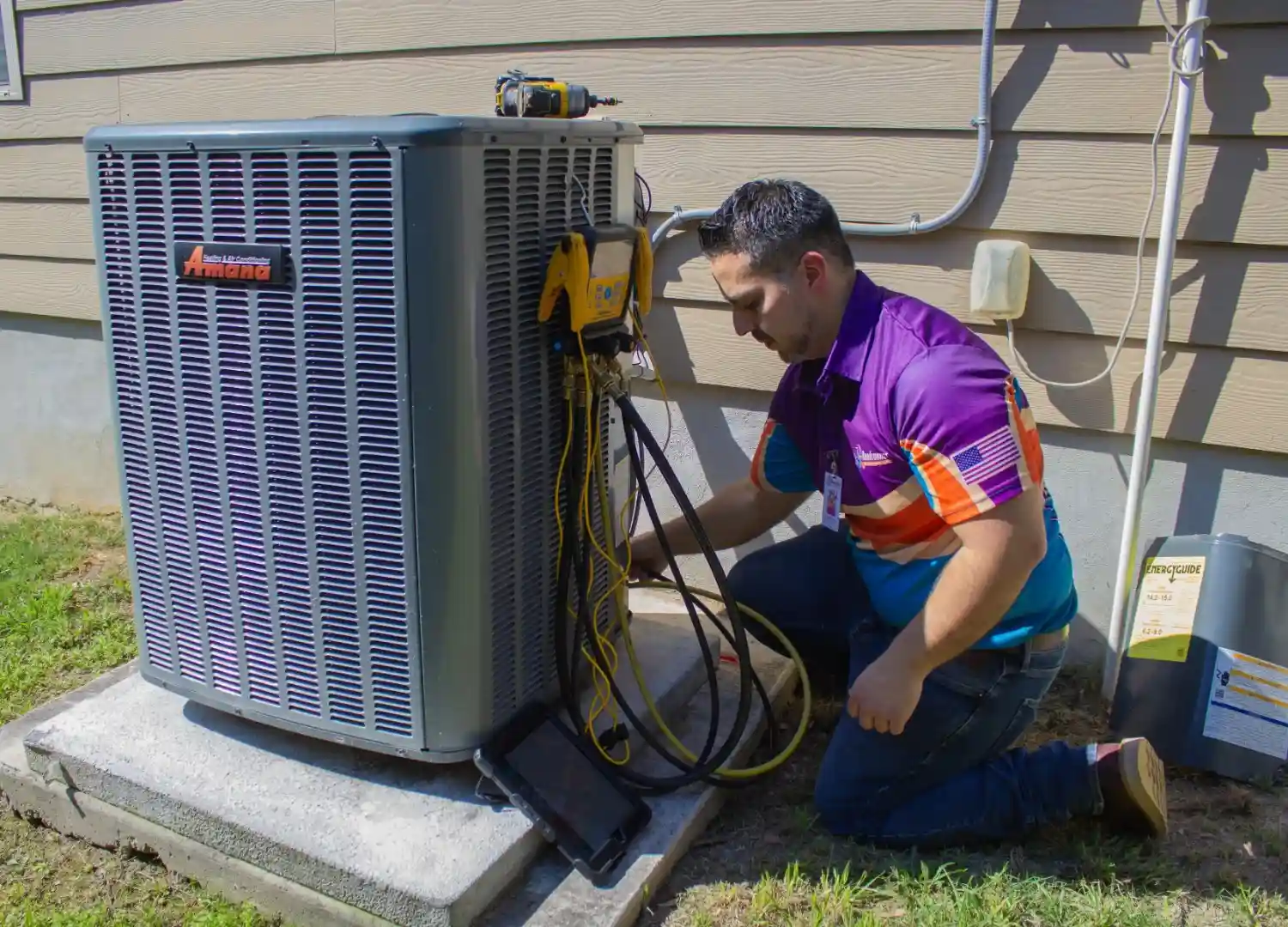 A technician in a purple and orange shirt services an outdoor AC unit