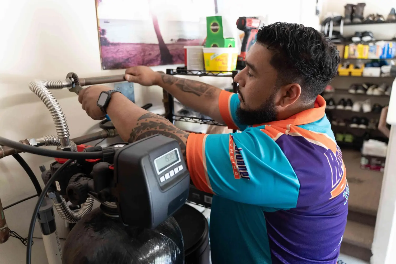 A plumber with tattoos on his arms adjusts a water filtration system