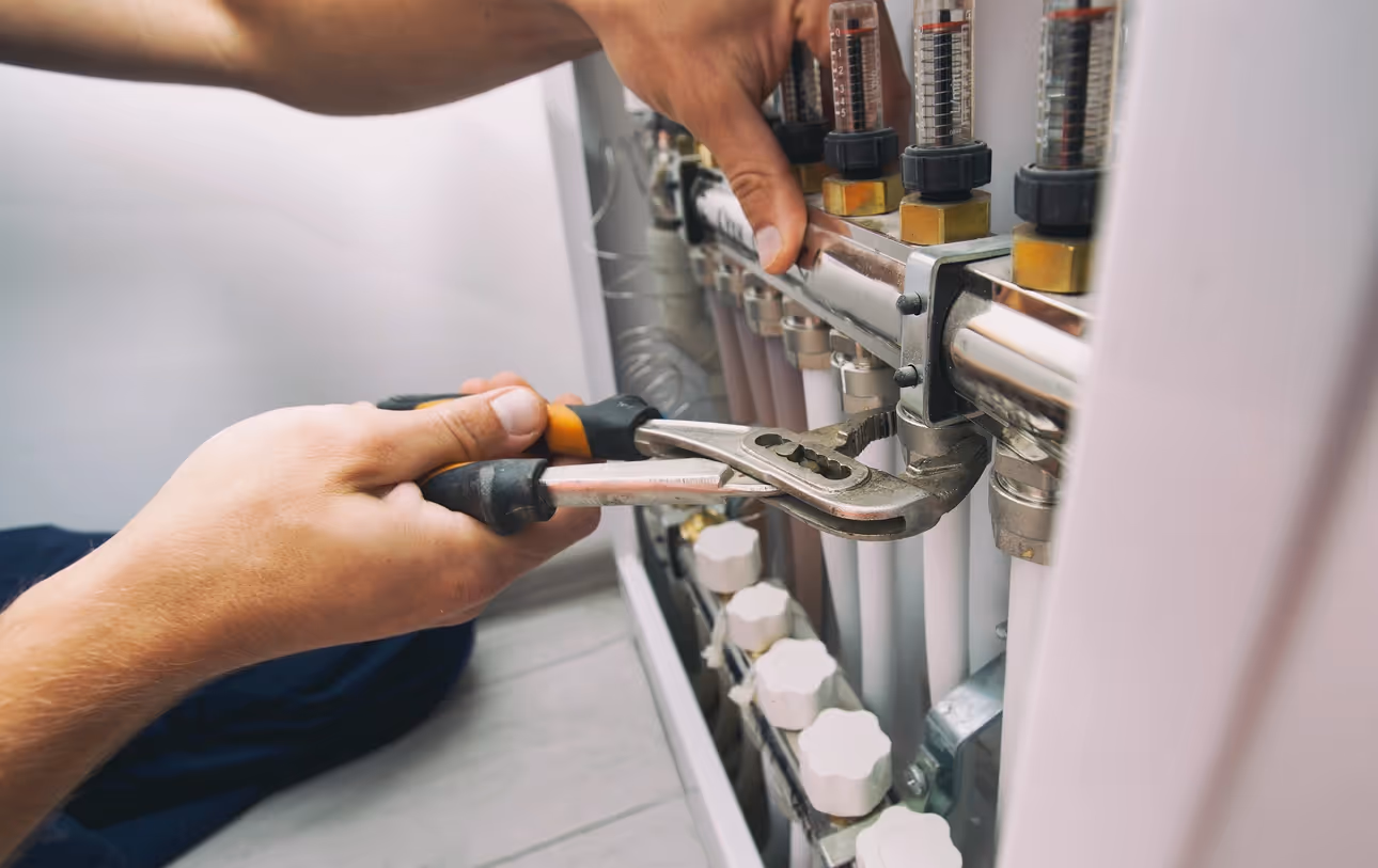A person adjusts pipes in a plumbing system using a wrench, focusing on gauges and valves.