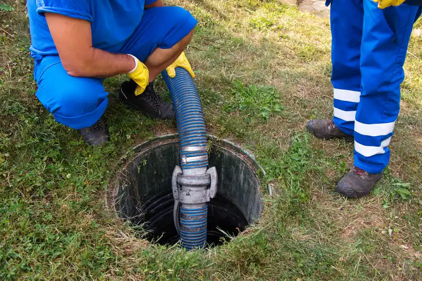 Septic service workers pump a tank in a yard.