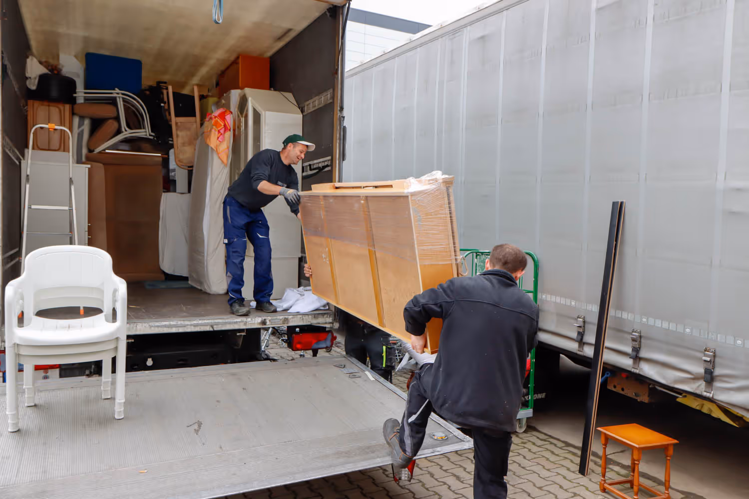 GRAVITAS Mitarbeiter bei einer Wohnungsauflösung, Entrümpelung oder Kleintransporter Seniorenumzug räumen Möbel aus dem Lieferwagen aus.