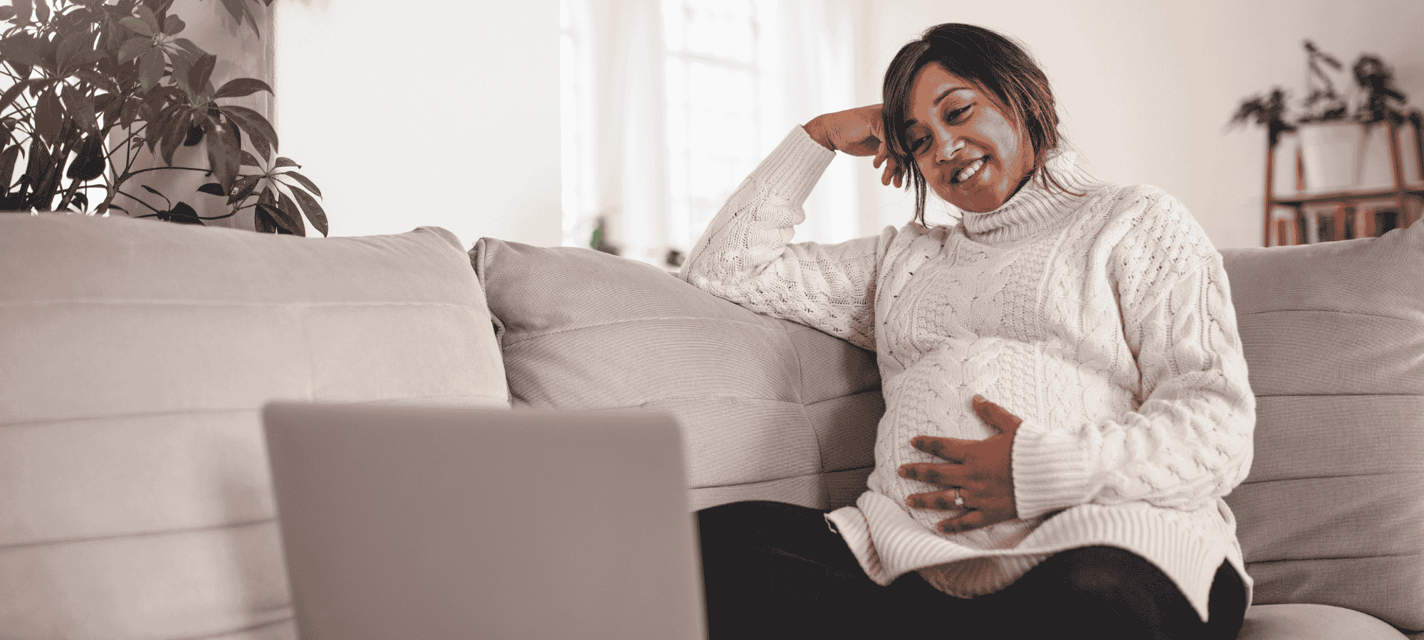 A pregnant person on the sofa by a laptop