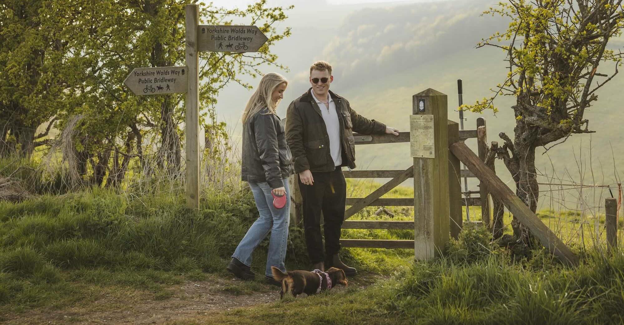couple and dog walking through a gate on a forest path