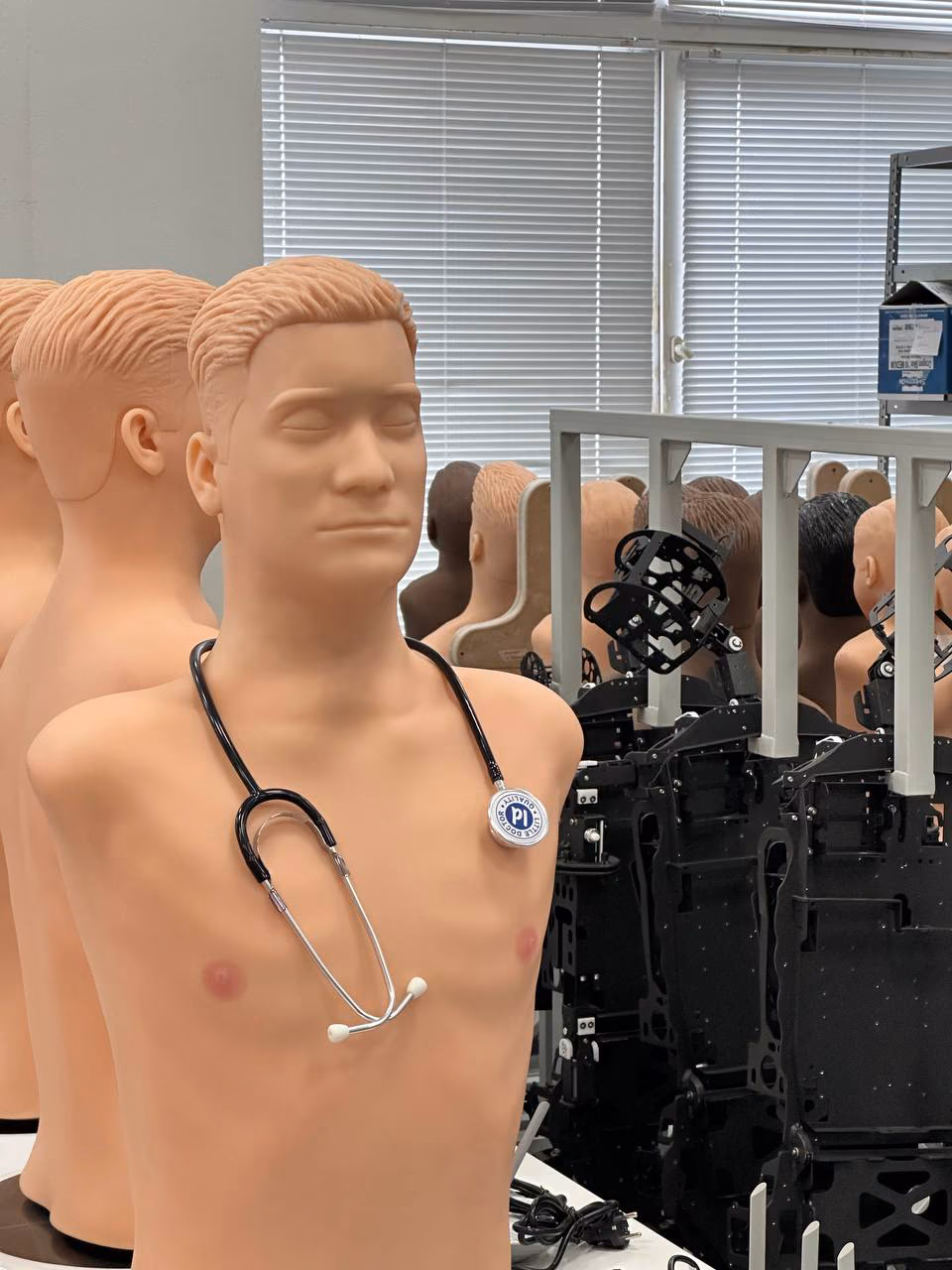 A torso simulator with a stethoscope, robot-patient frames waiting for assembly behind it