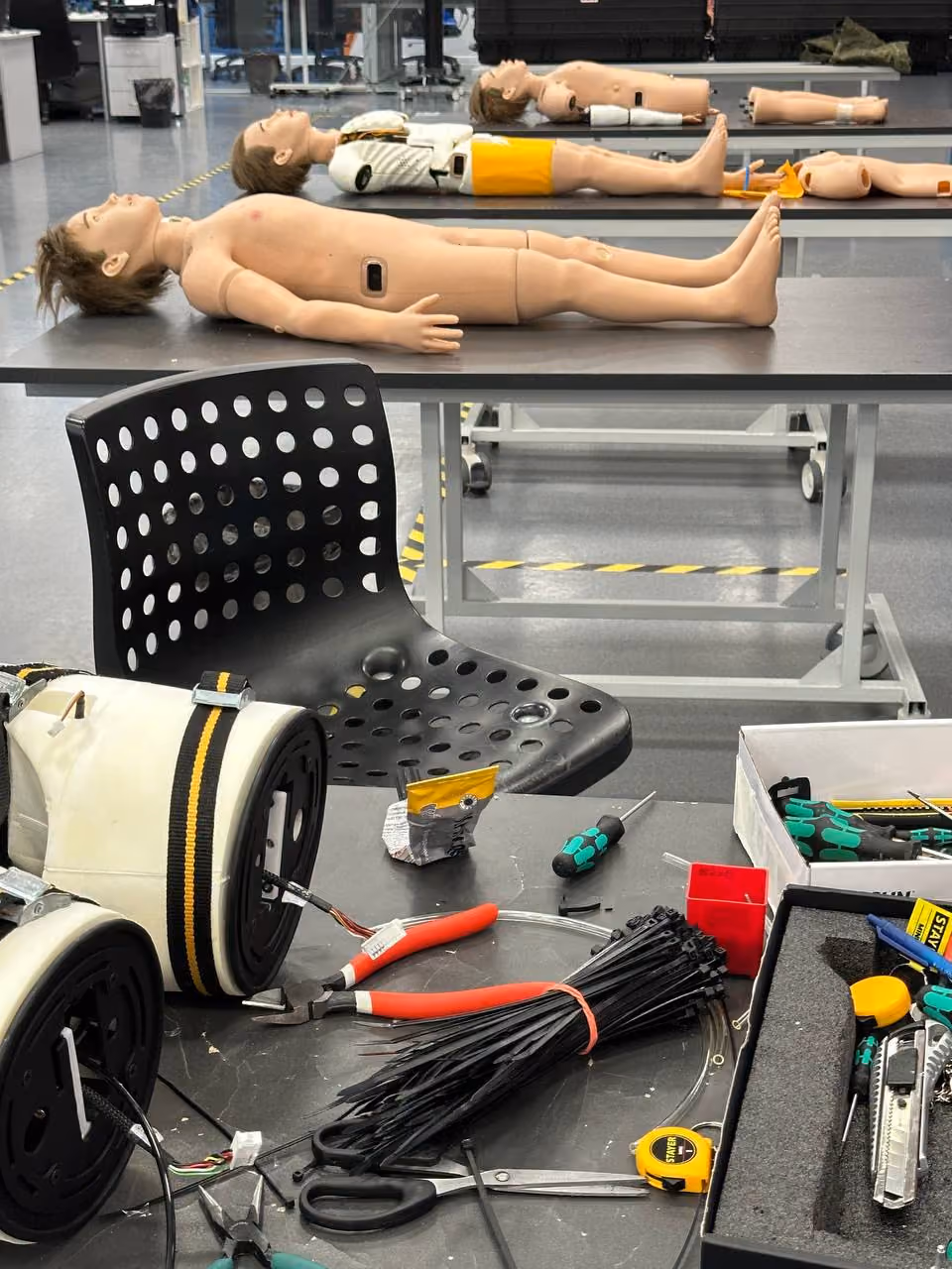 Pediatric patient simulators on assembly tables, tools on the workbench in front