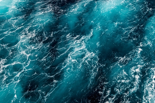 Turbulent ocean water with visible waves and foam under sunlight.