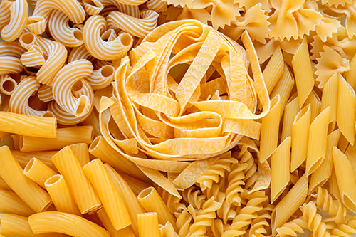 Variety of dry pasta types including penne, farfalle, fusilli, rigatoni, and fettuccine in the center.