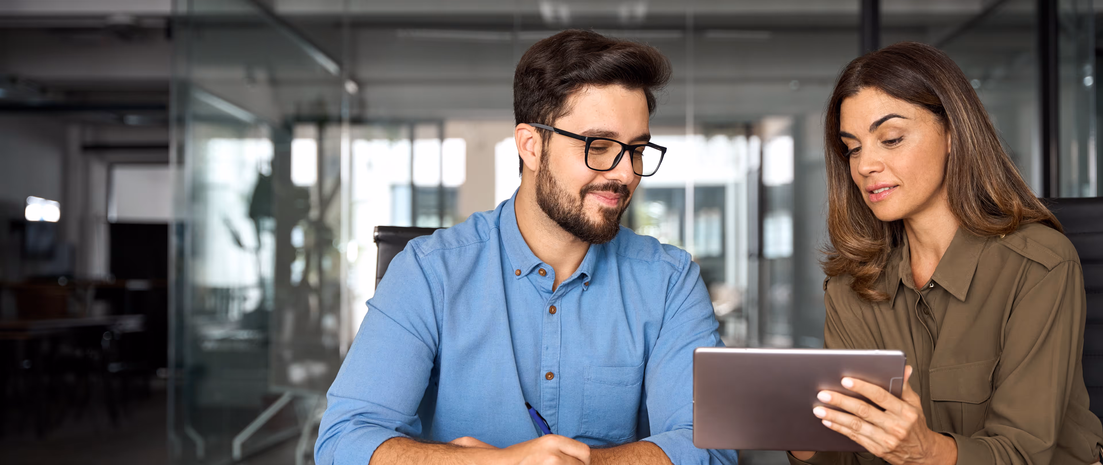 Two colleagues reviewing content on a tablet together in a modern office.