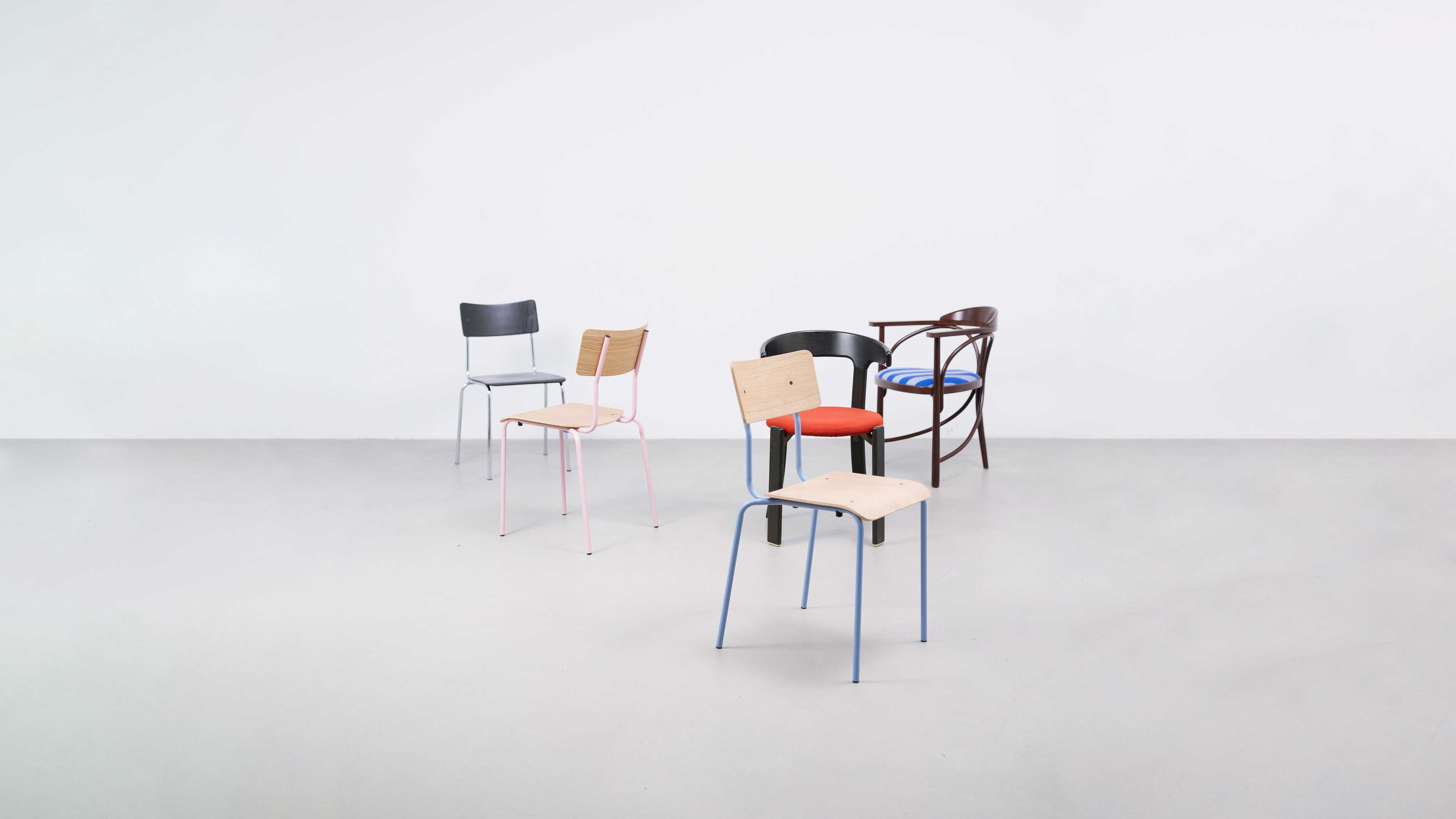 Vier Stühle mit verschiedenen Designs und Materialien stehen auf grauem Boden vor weißer Wand.