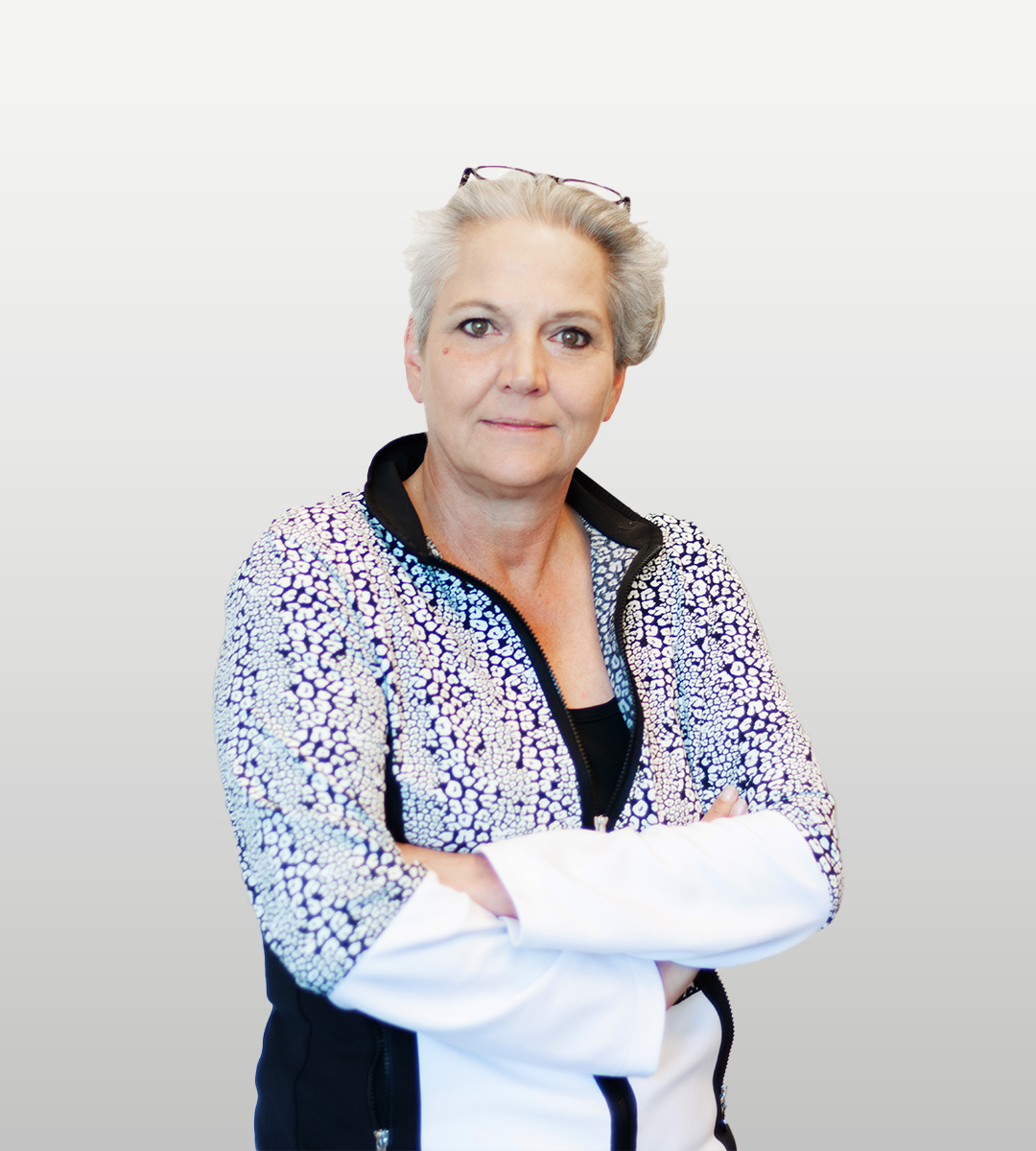 Frau mittleren Alters mit grauen Haaren und gemusterter Jacke vor hellem Hintergrund.