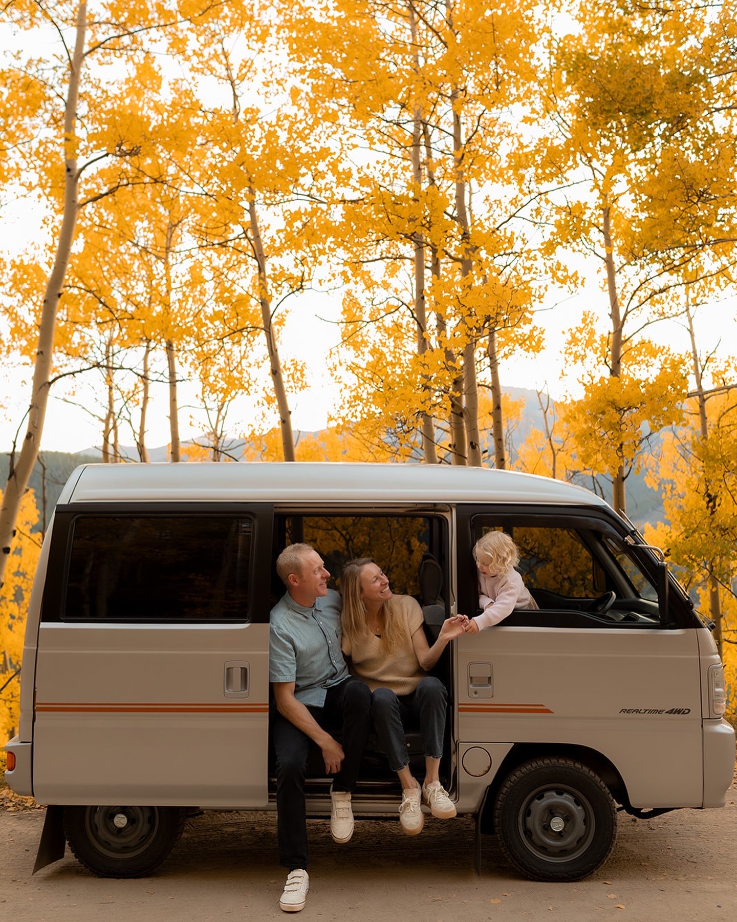 Young family sitting in a van on a dirt road surrounded by yellow Aspen trees