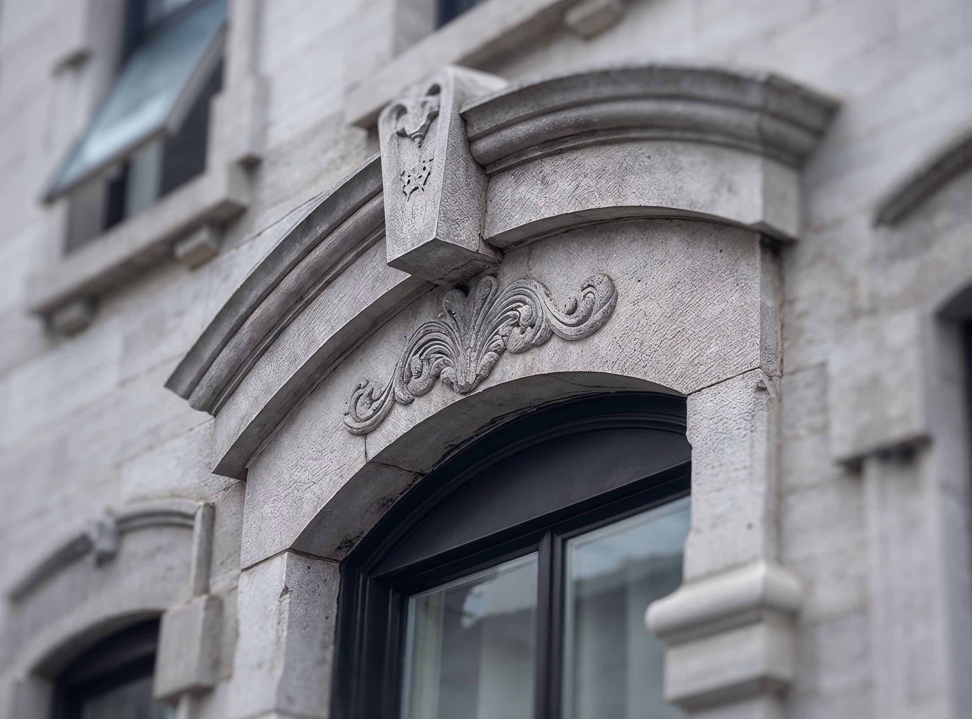 Close-up of a stone building facade with an ornate arched window frame and decorative carving.